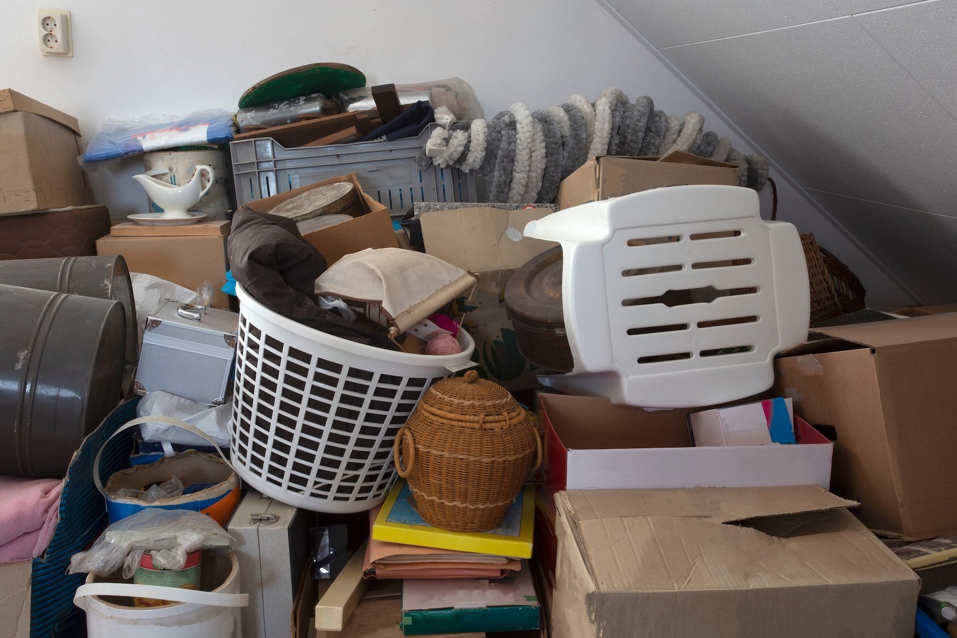 Cluttered attic storage area with stacked boxes, laundry baskets, blankets, and household items.