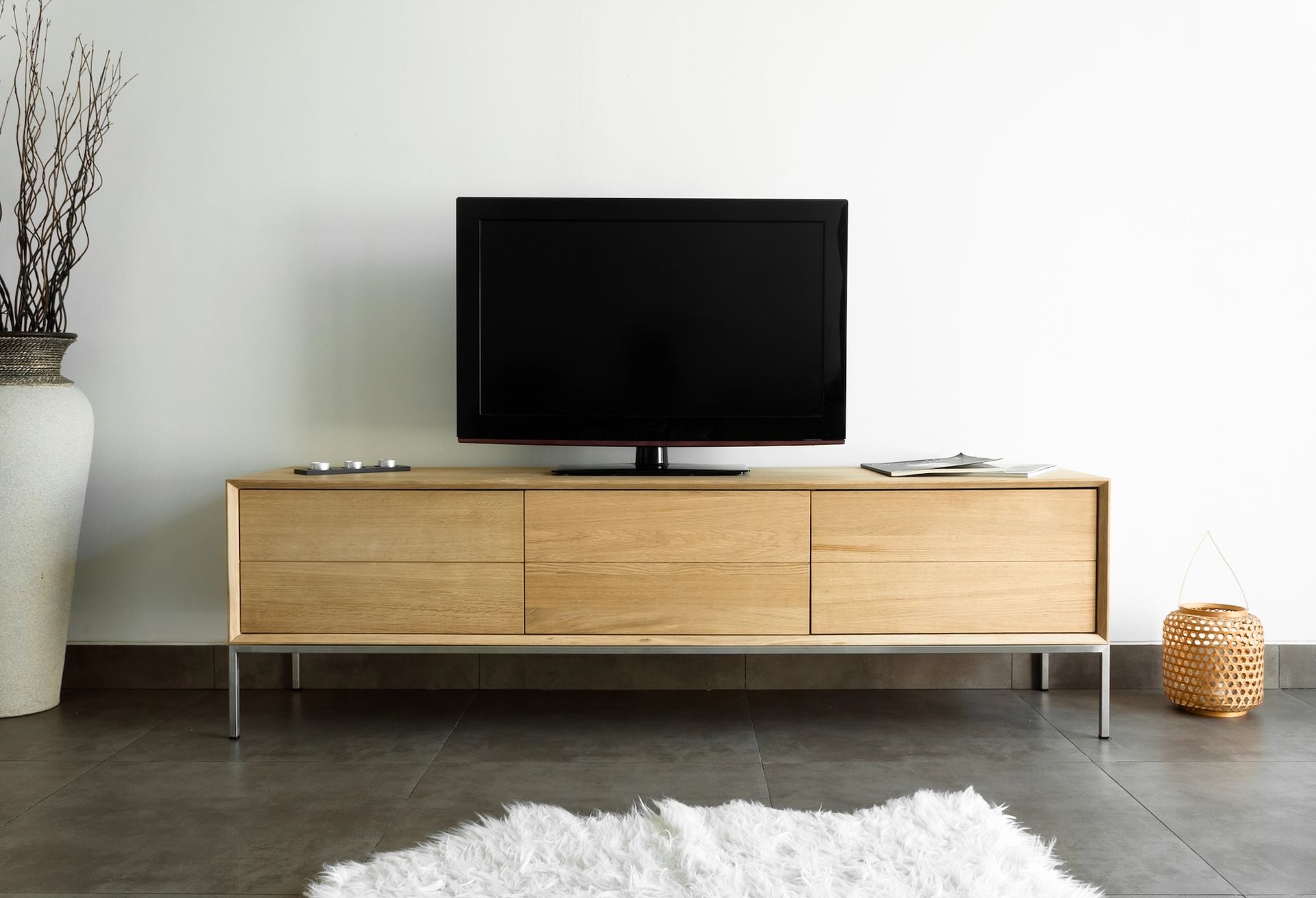 Minimal living room with a black TV on a light wood console against a white wall