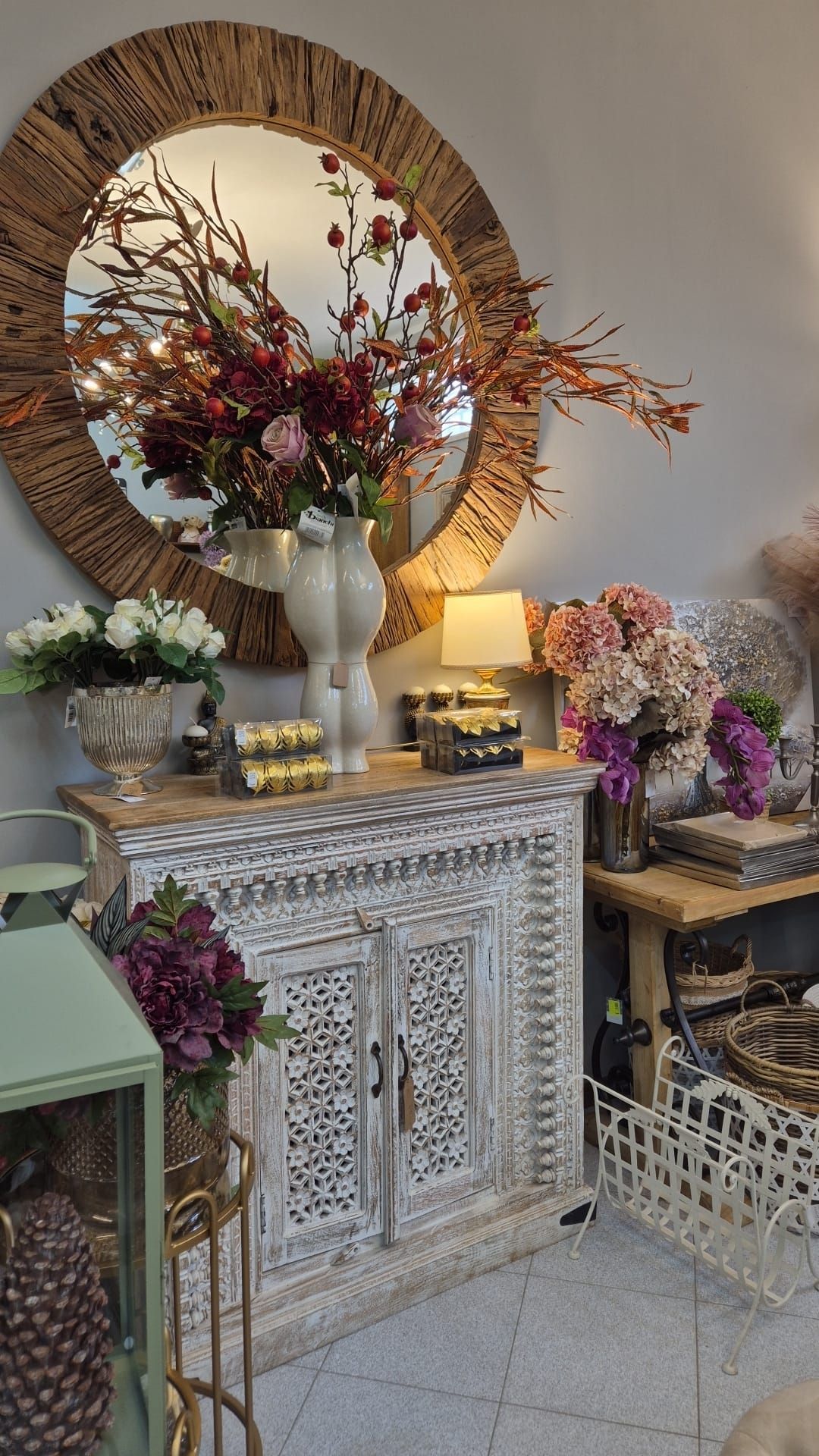Un mobiletto decorativo con ante intagliate è posto davanti a uno specchio decorato con composizioni floreali e decorazioni.