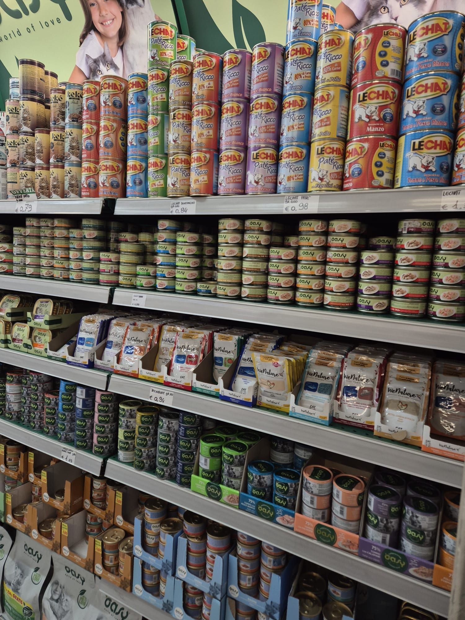 Scaffali pieni di vari prodotti alimentari in scatola e confezionati per gatti in un supermercato.