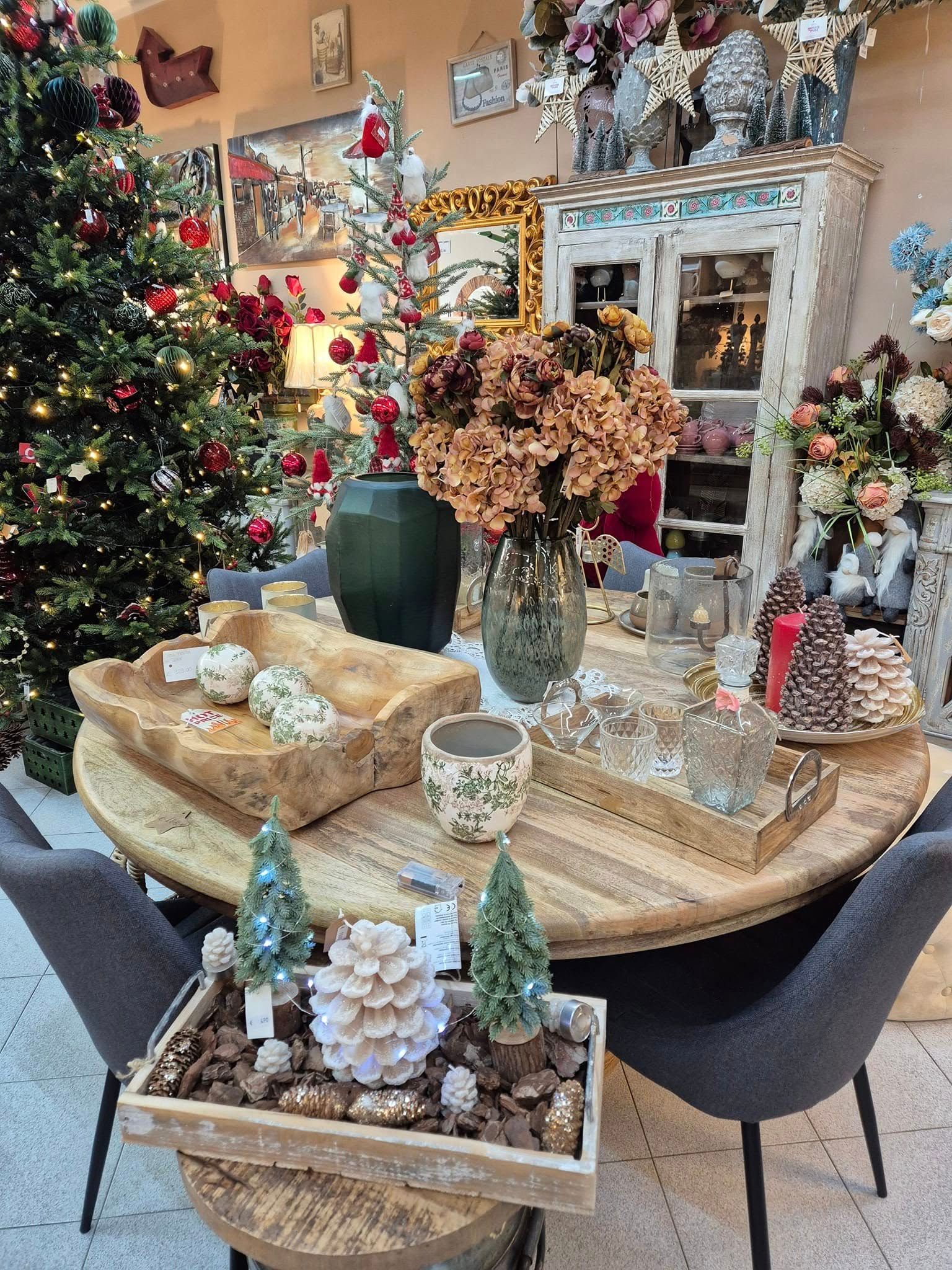 Un tavolo rotondo decorato, tra cui fiori e alberi in miniatura, in un negozio di decorazioni natalizie.