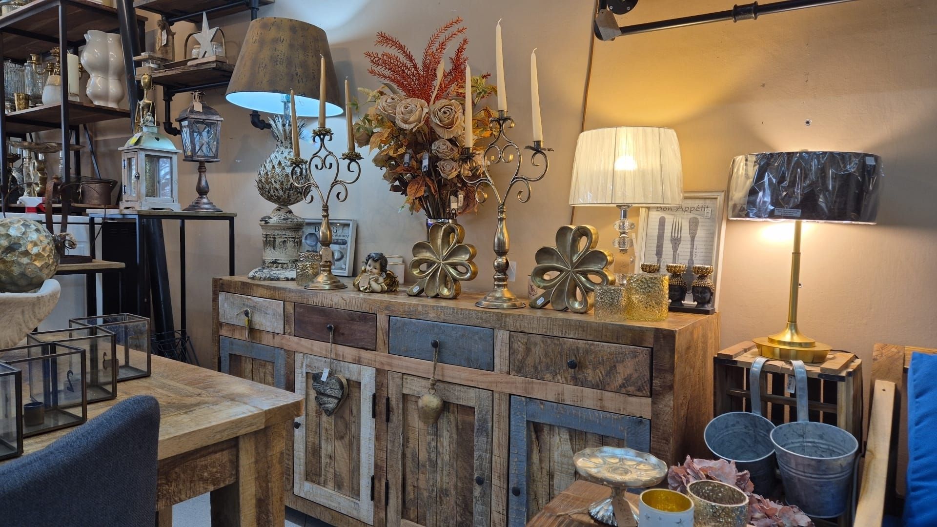 Una vetrina rustica in legno che espone oggetti decorativi come lampade, portacandele e fiori in un ambiente da negozio.