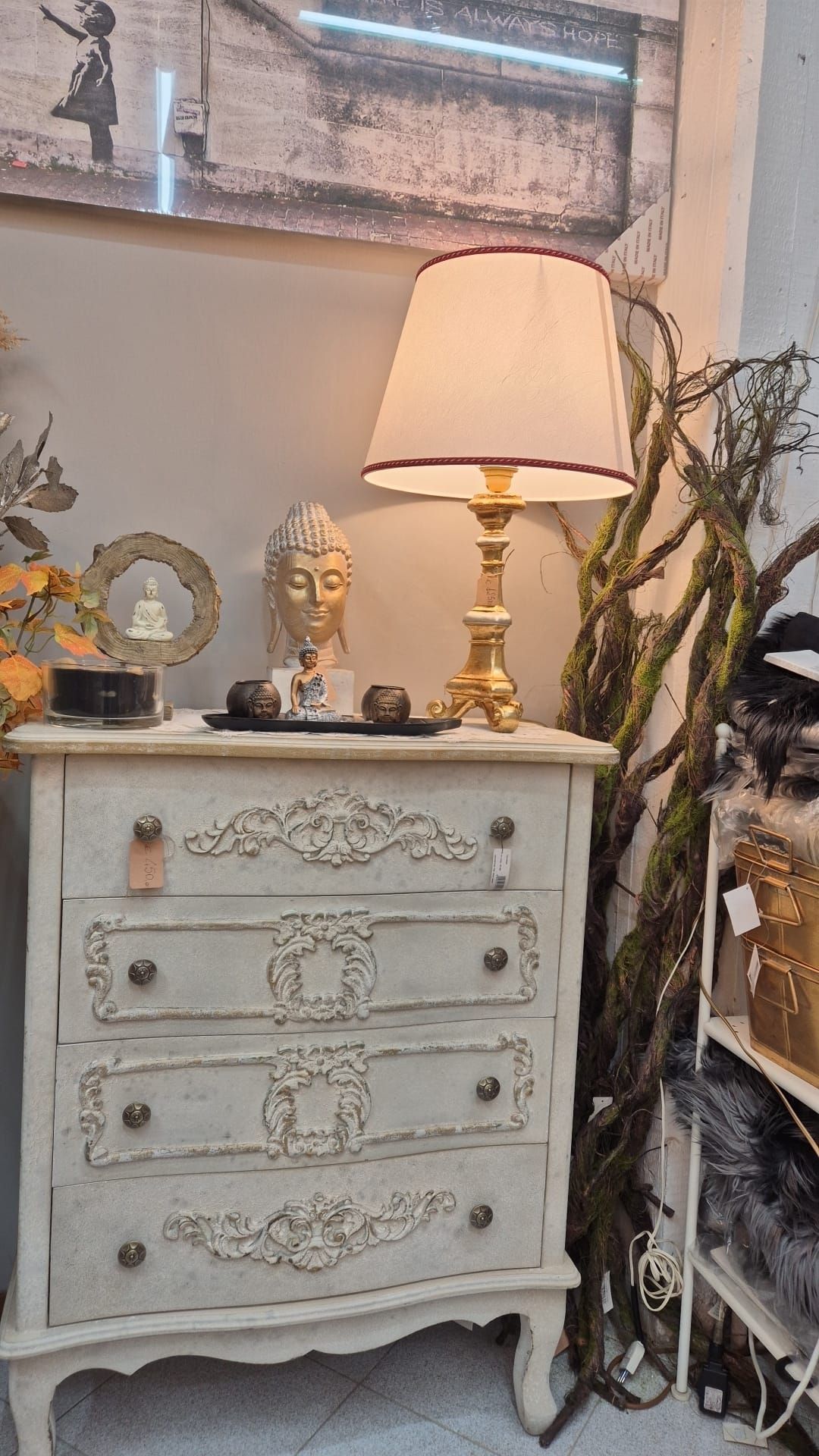 Una cassettiera bianca decorata con una lampada, una testa di Buddha e rami. Decorazione d'interni.