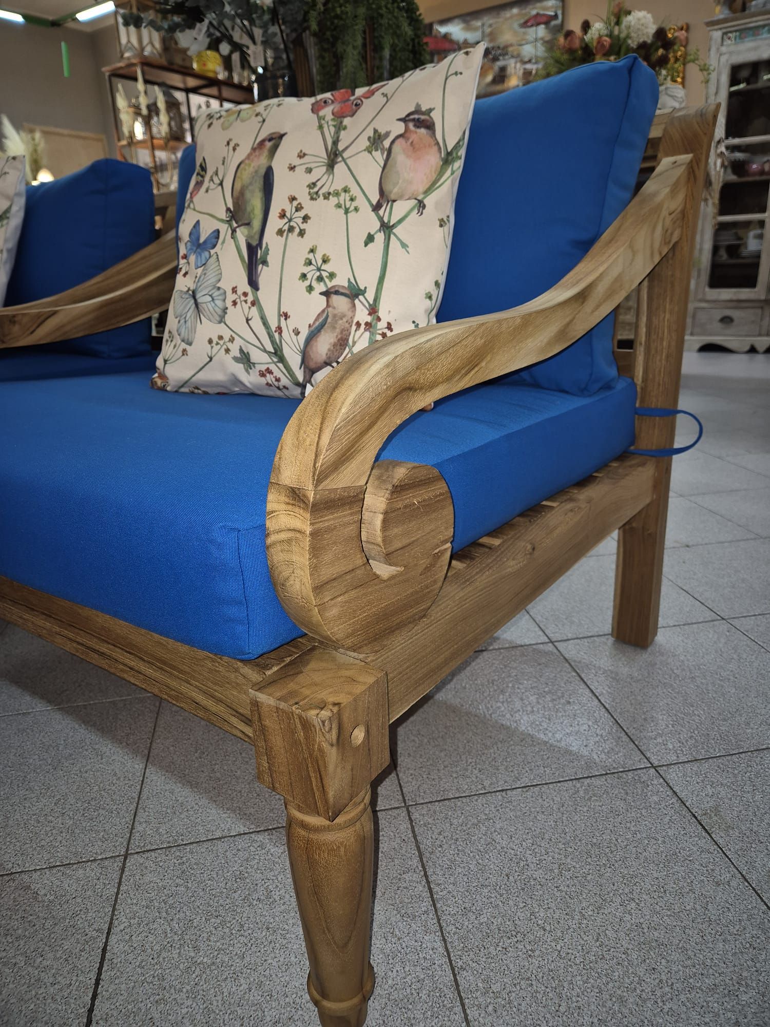 Divano da esterno in legno con cuscini blu e cuscino con stampa di uccelli.