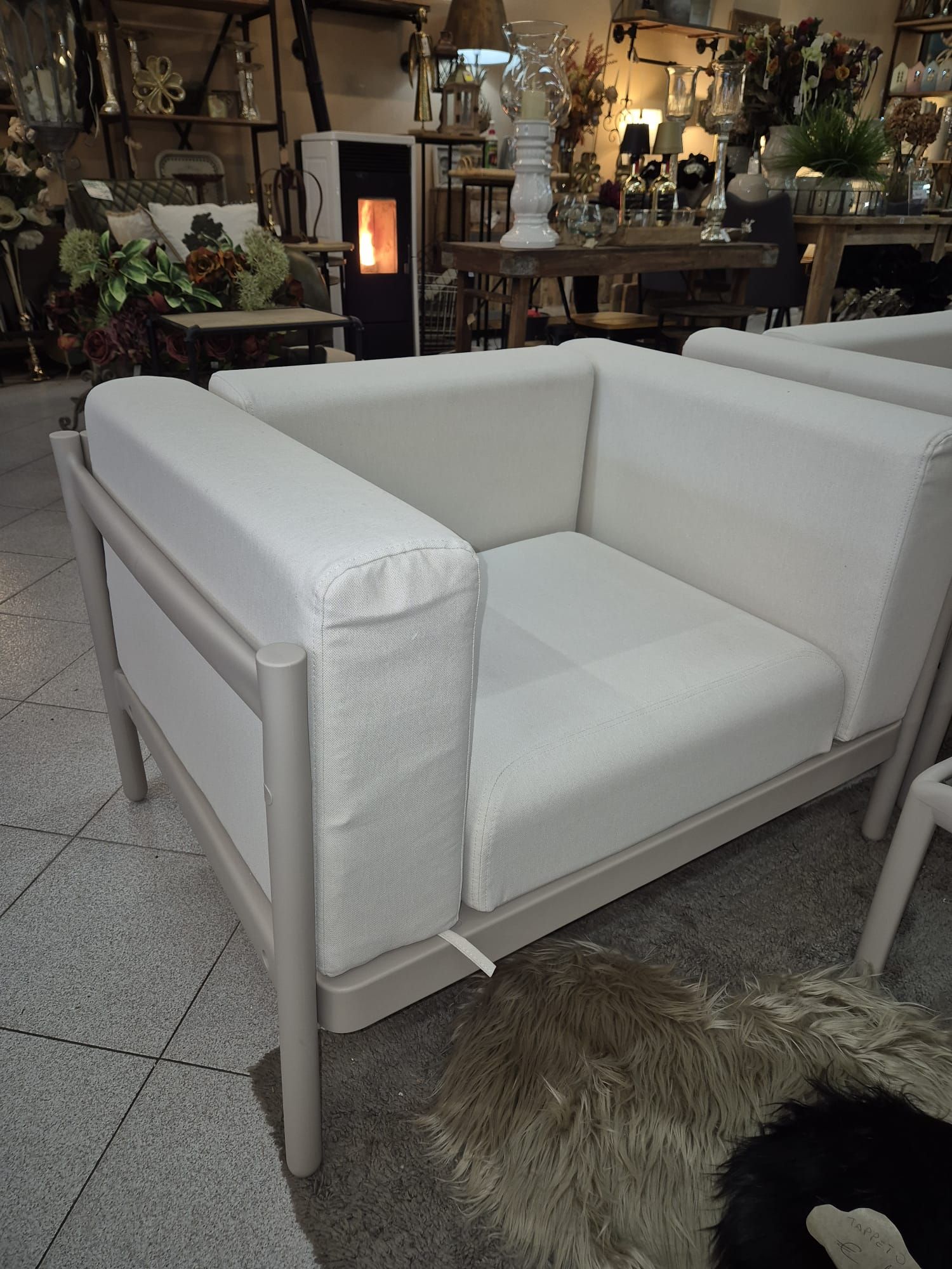 Sedia da esterno moderna color crema con struttura grigio chiaro, posizionata in un negozio.