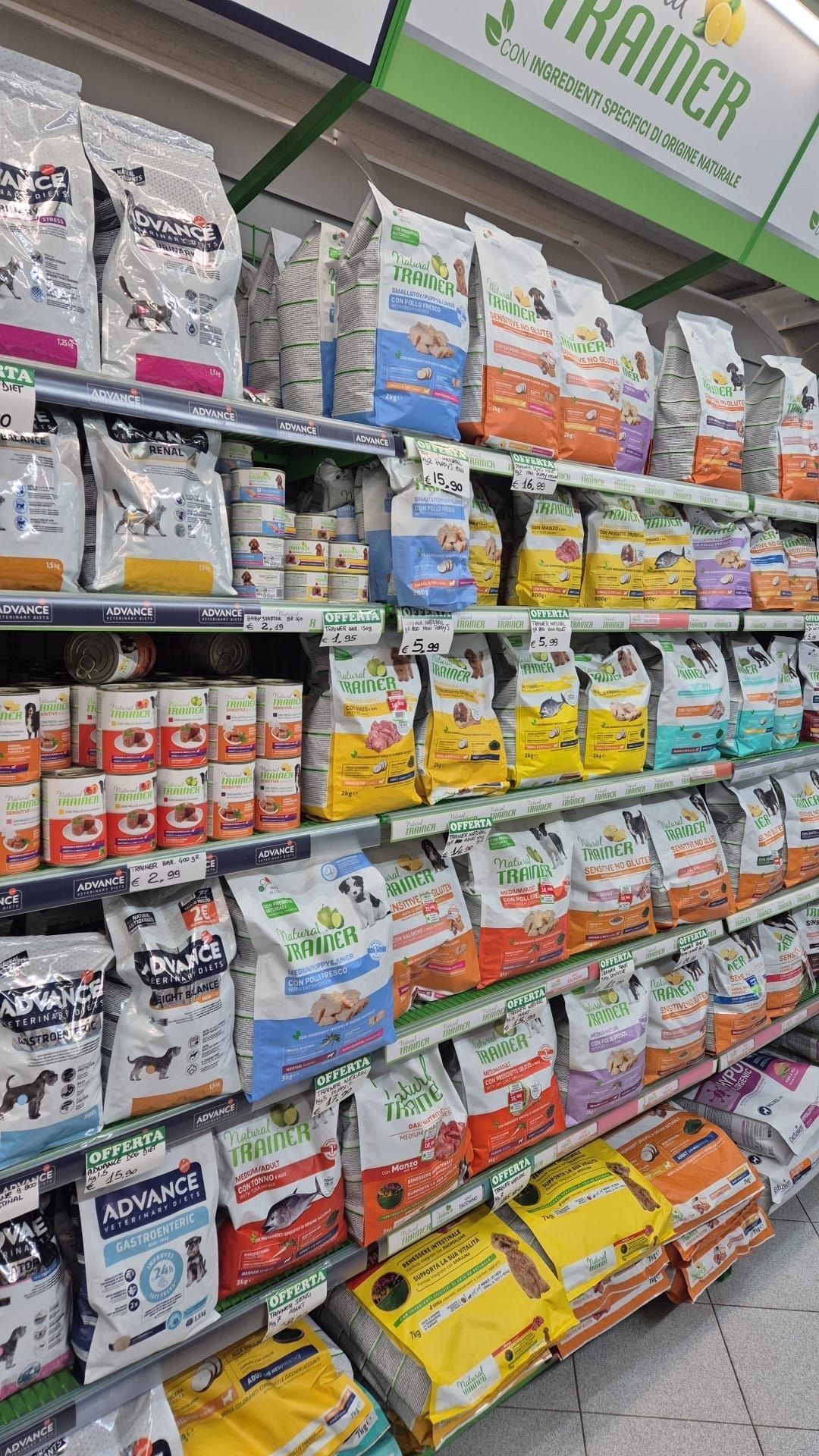 Scaffali pieni di cibo per cani di varie marche in un supermercato.