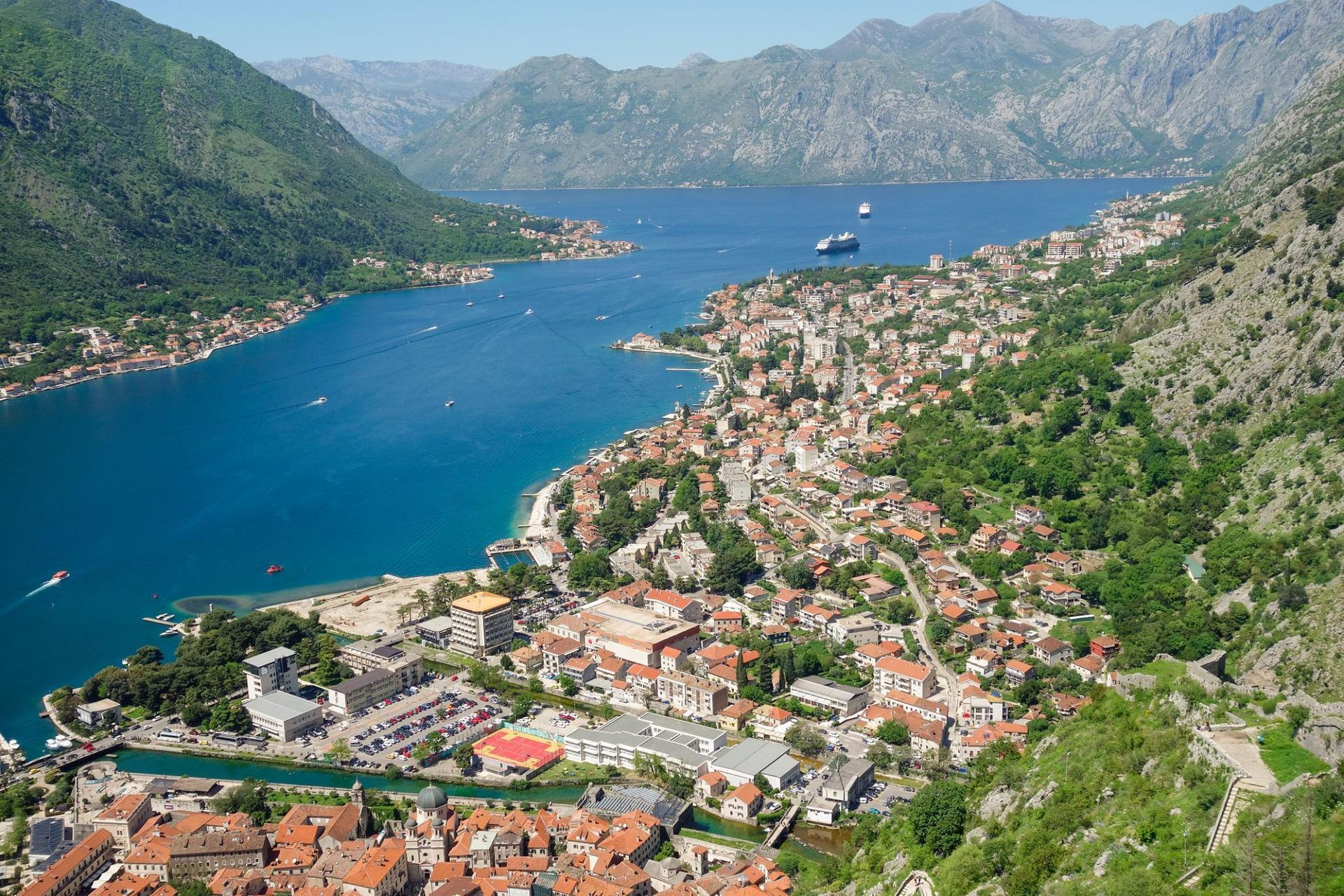 Kotor, Montenegro A coastal town beside a blue bay, with terracotta roofs and green mountains rising around it.