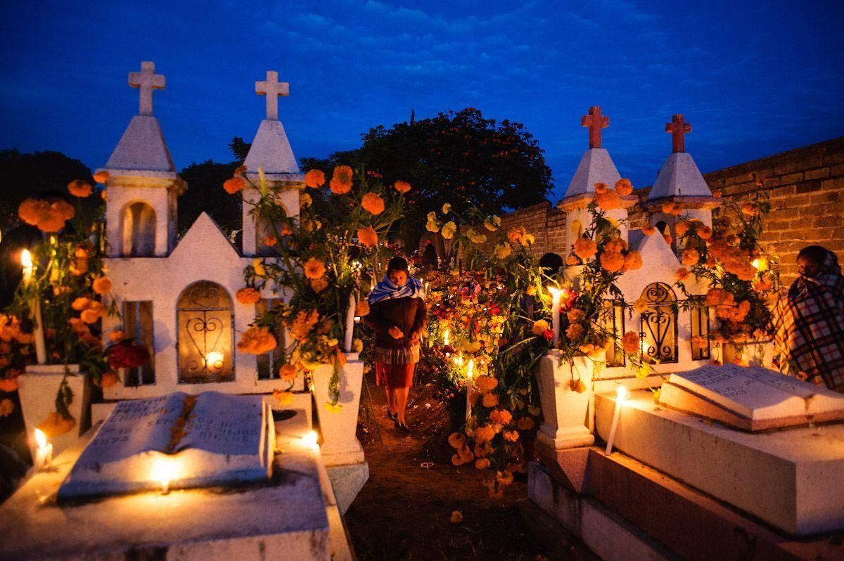 Dia de Muertos in Oaxaca Candlelit cemetery altar with white tombs, flowers, and crosses at dusk under a blue sky