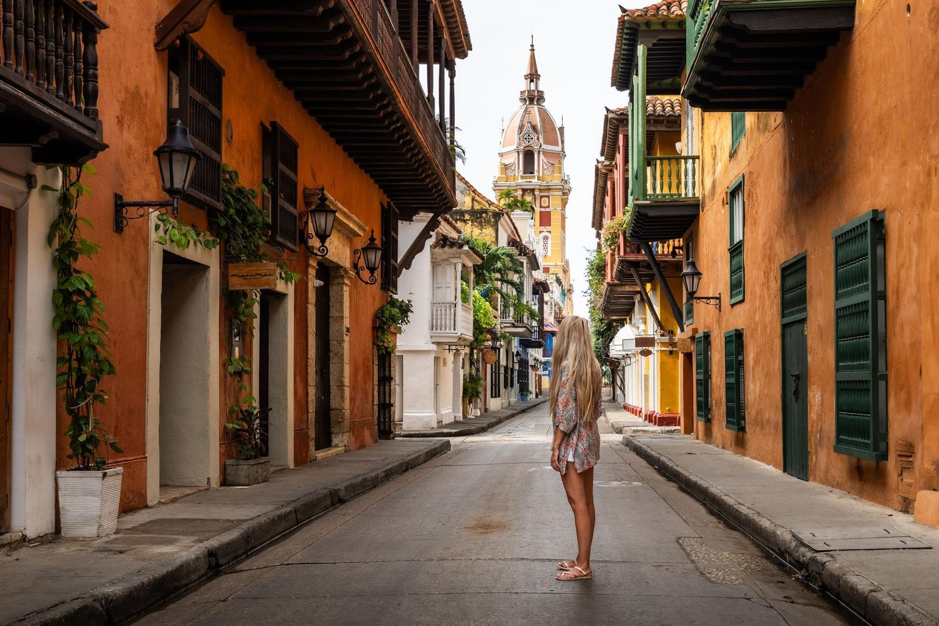 A person stands in a narrow colonial Colombian street lined with orange buildings and green shutters.
