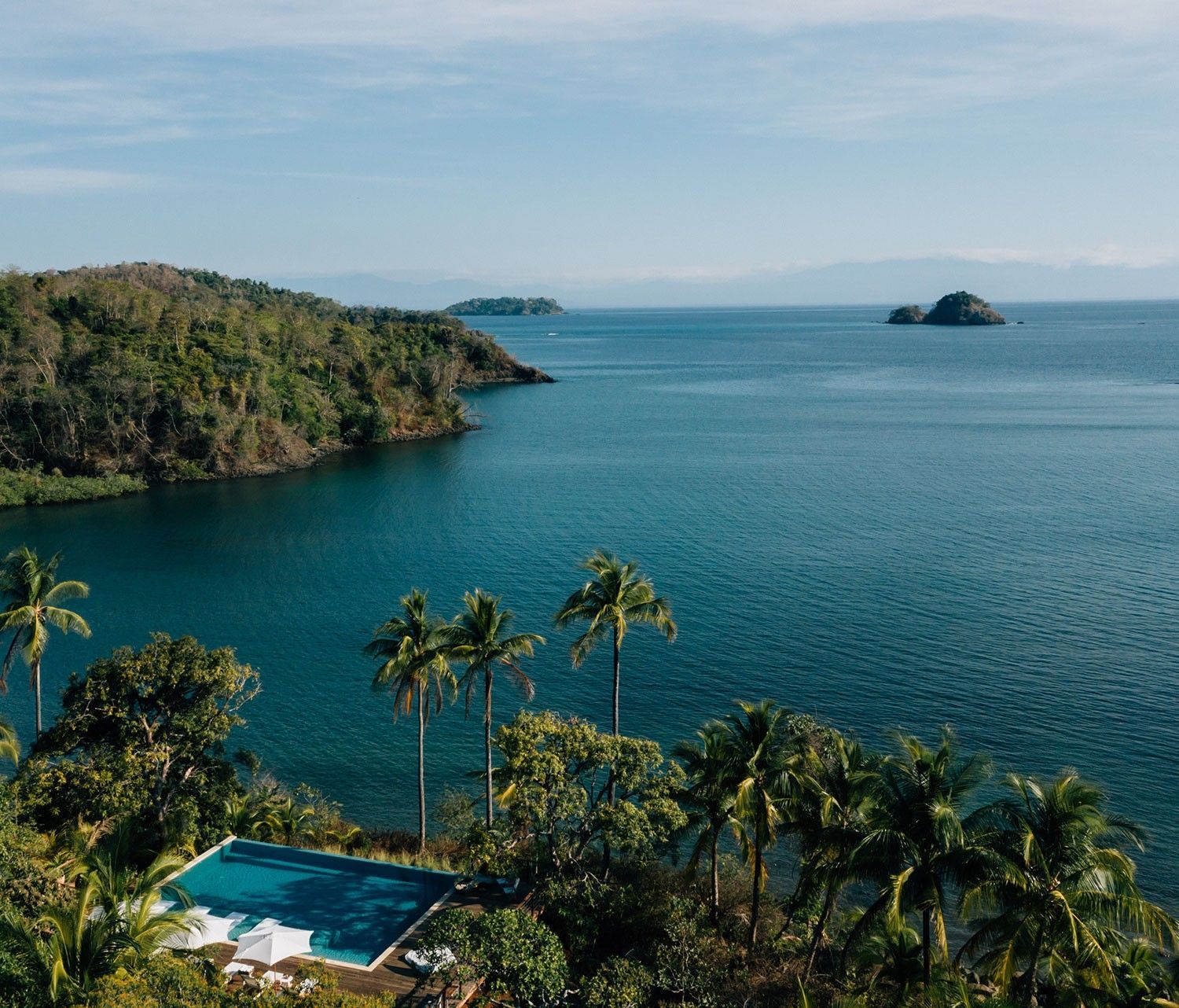 Islas Secas, Panama Tropical bay with calm blue water, palm trees, and a pool overlooking a green shoreline.