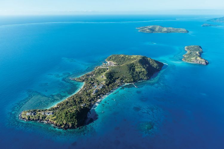Kokomo Private Island, Fiji Aerial view of a lush tropical island surrounded by vivid turquoise and deep blue ocean.