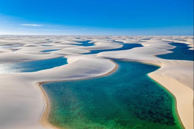 Aerial view of turquoise water winding through white sand dunes under a clear blue sky