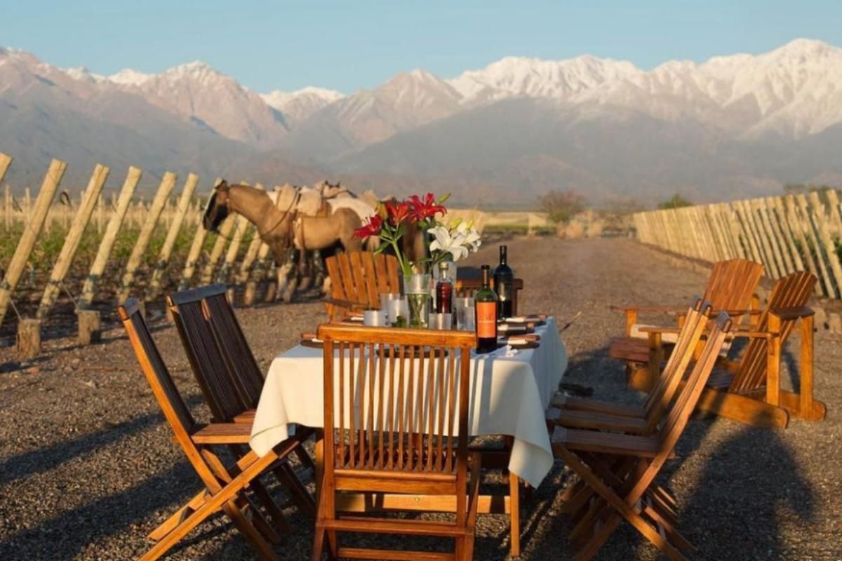 Outdoor dining table with chairs on a vineyard terrace, overlooking the Andes Mountains at sunset