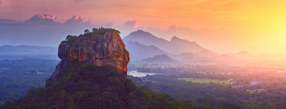 Sunrise over a Sigiriya (Lion Rock) with misty blue valleys and warm orange sky