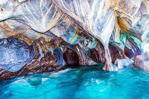 Colorful marble cave walls above bright turquoise water in a narrow grotto