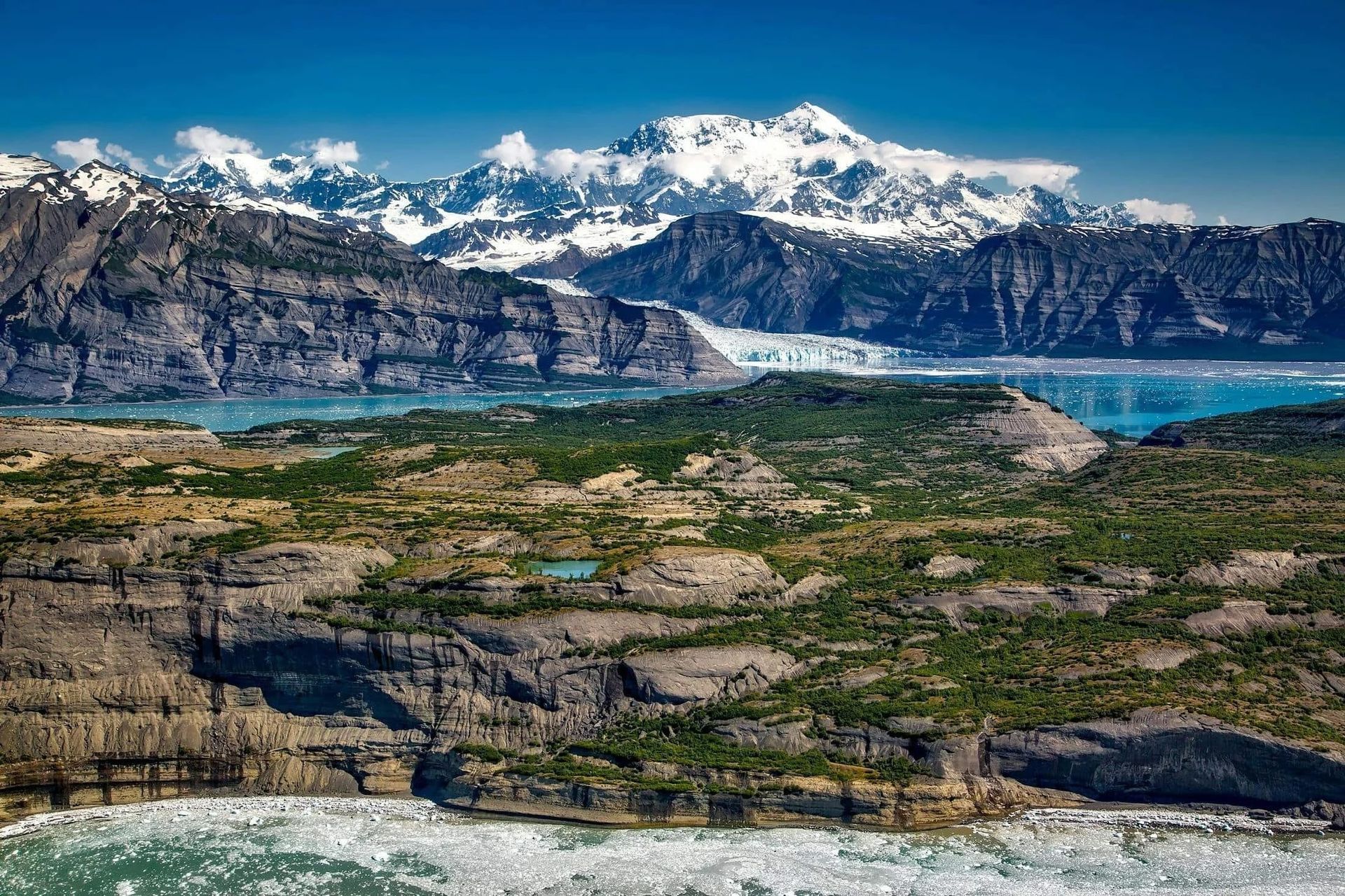 Snowy mountains above a turquoise lake and rugged green valley under a clear blue sky
