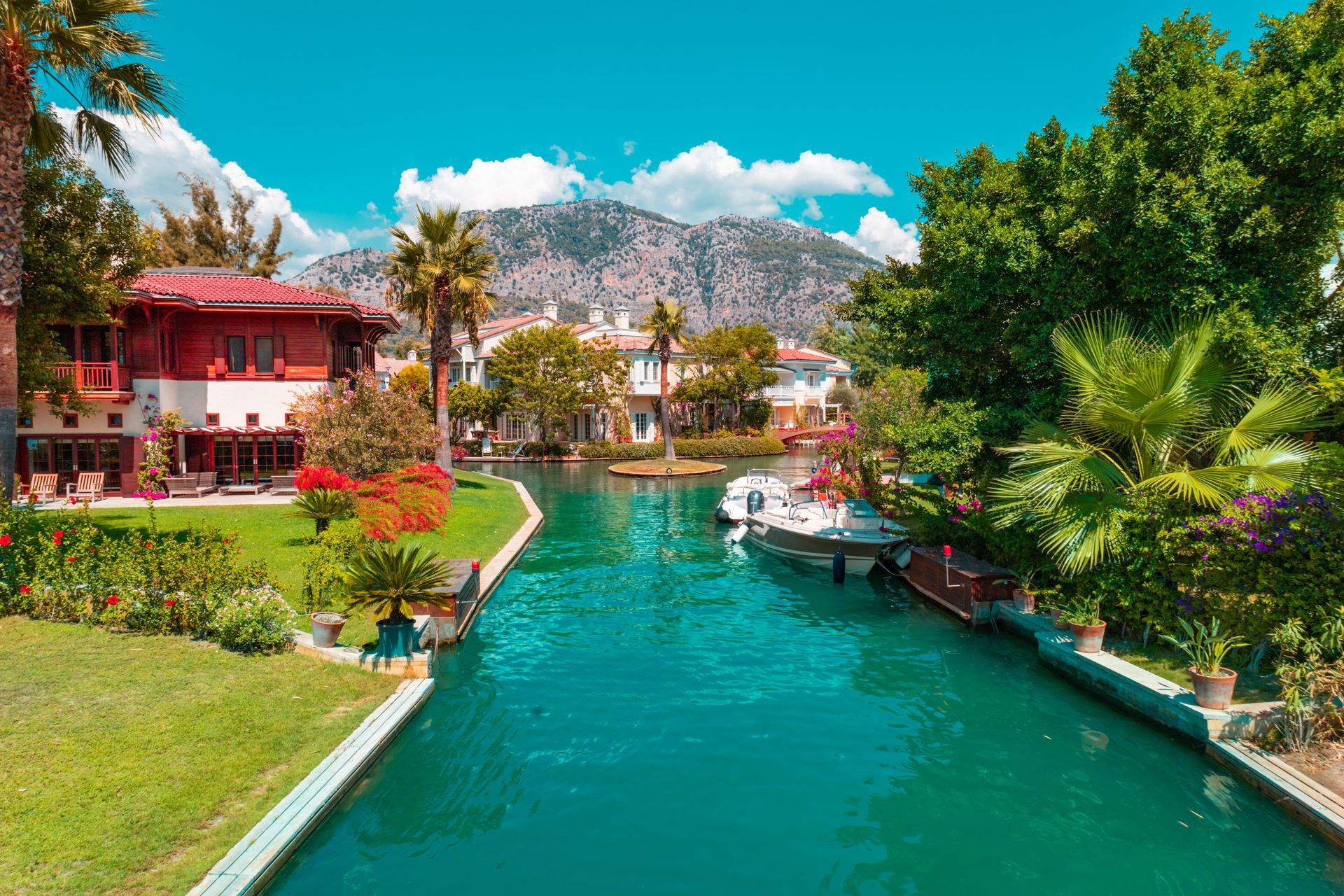 Tropical canal lined with colorful villas, lush greenery, and turquoise water under a bright blue sky