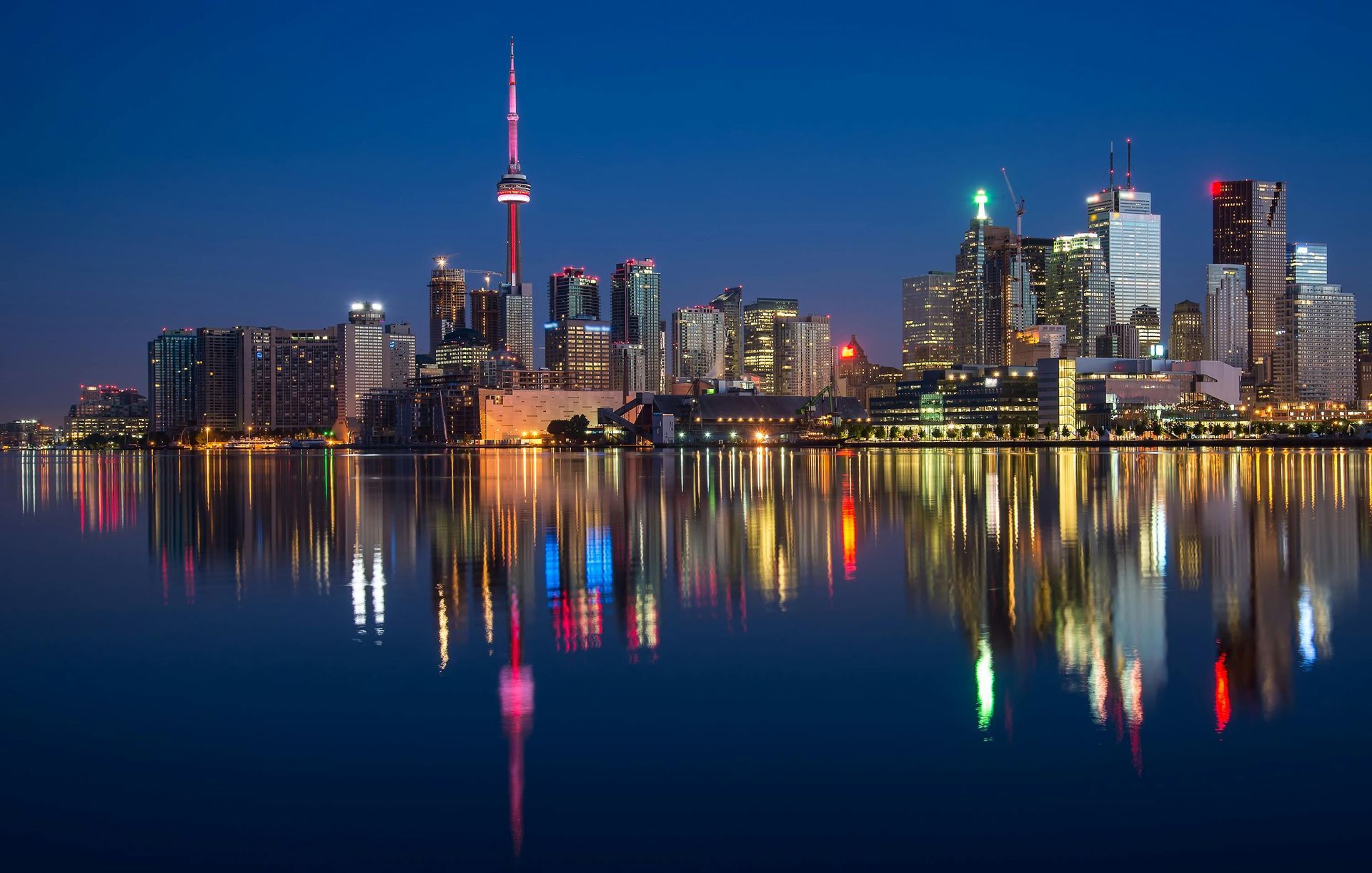 Toronto skyline at night, reflected in calm water. Illuminated buildings with bright lights.