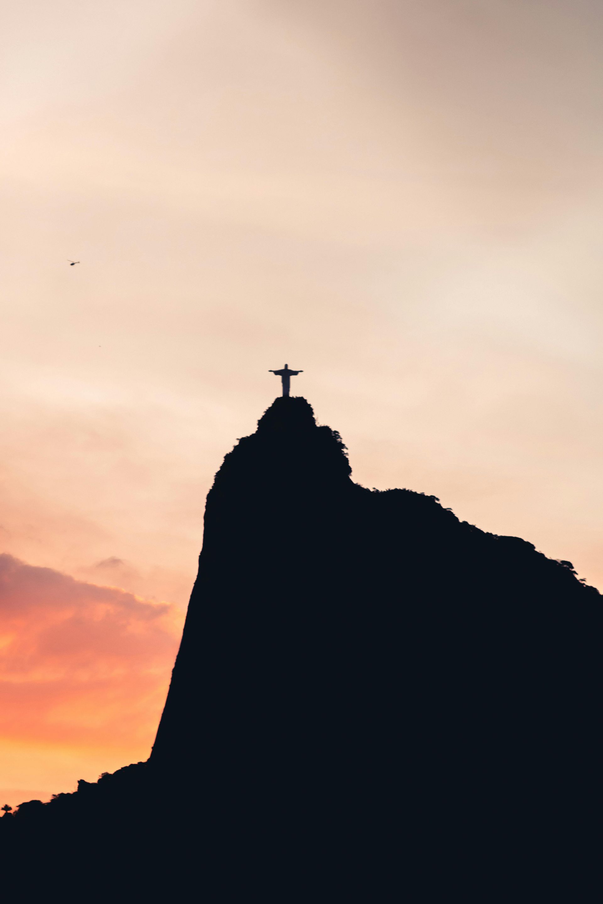 Silhouette of Christ the Redeemer statue atop Corcovado Mountain at sunset.