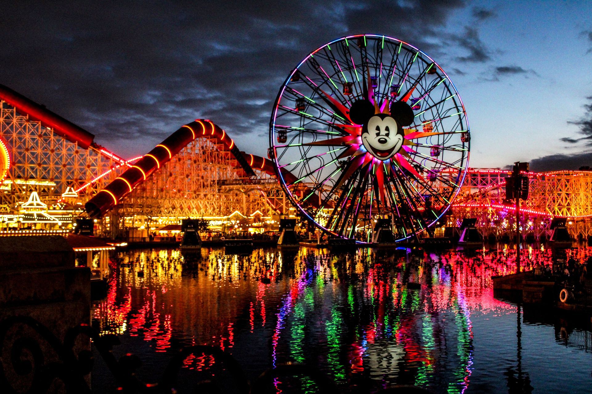 Colorful nighttime amusement park with a lit Ferris wheel and reflections on water