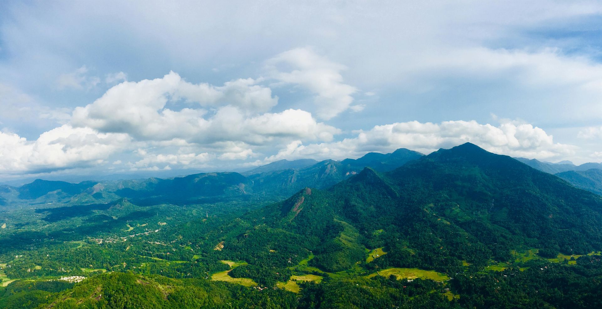 Green, forested mountains under a cloudy, blue sky.
