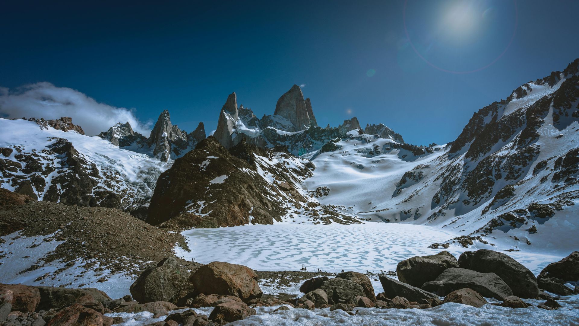 Snow-covered mountain range under a bright blue sky with sun.
