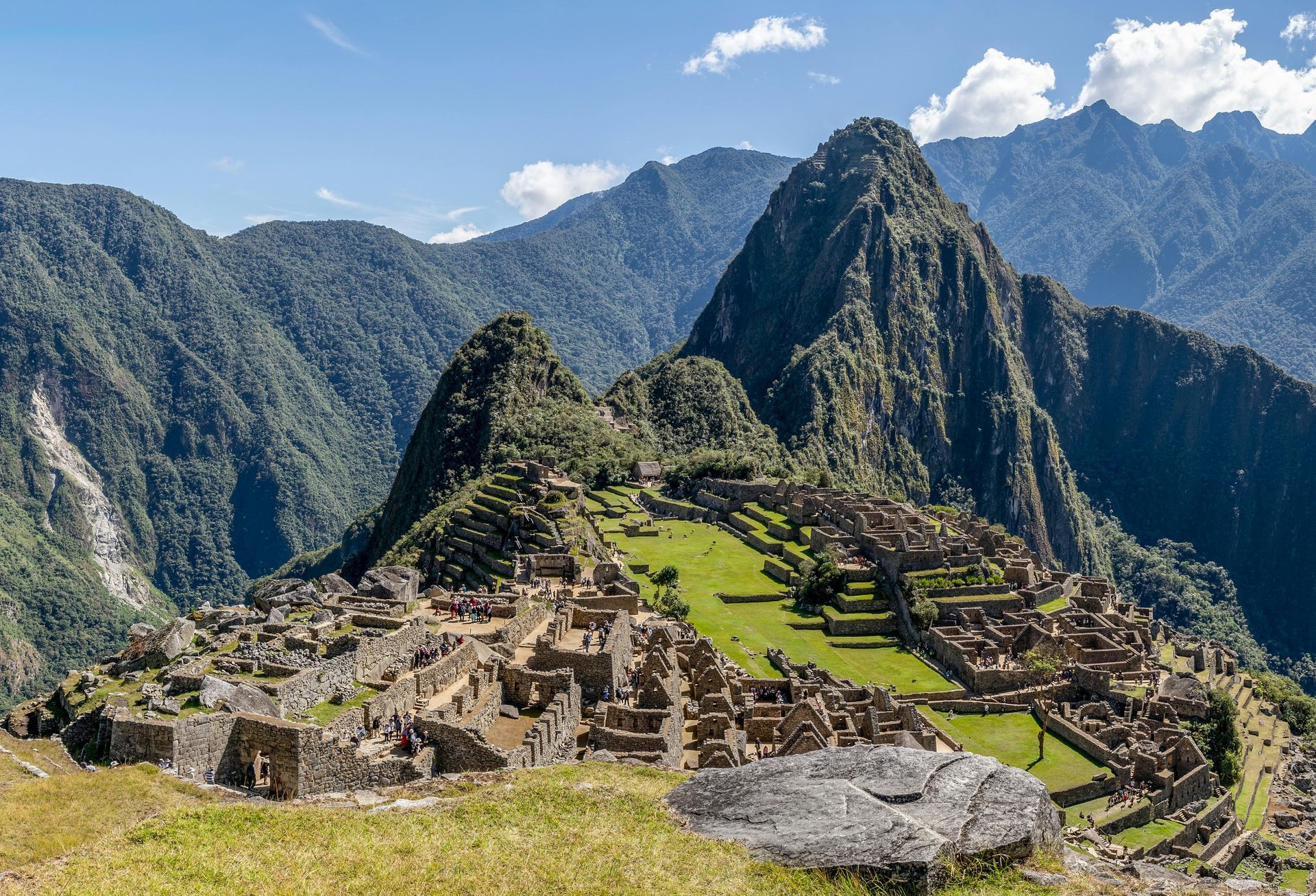 Machu Picchu ruins on a green mountainside beneath steep Andes peaks and a blue sky