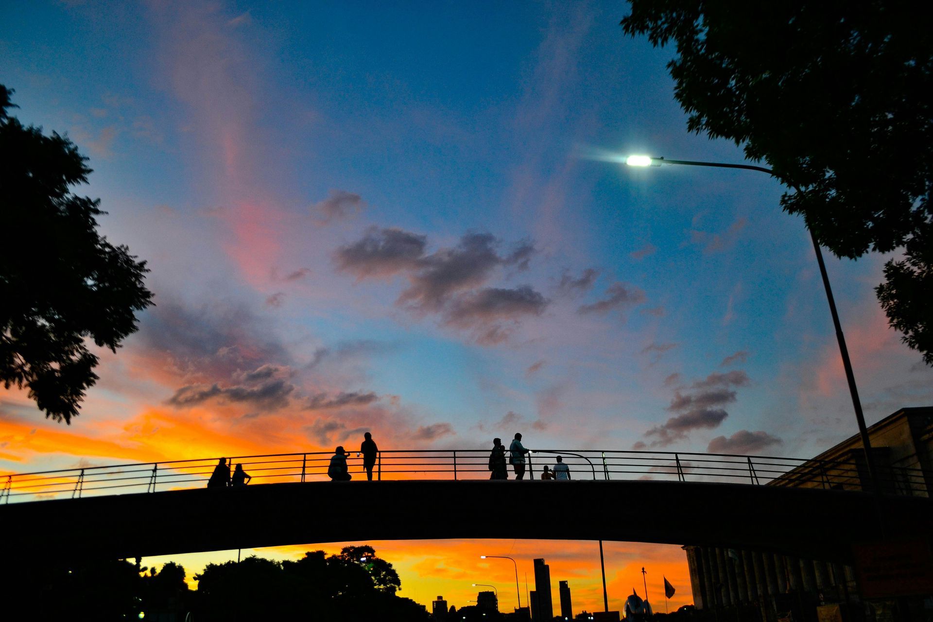 Silhouetted people on a bridge at sunset with orange, pink, and blue sky.