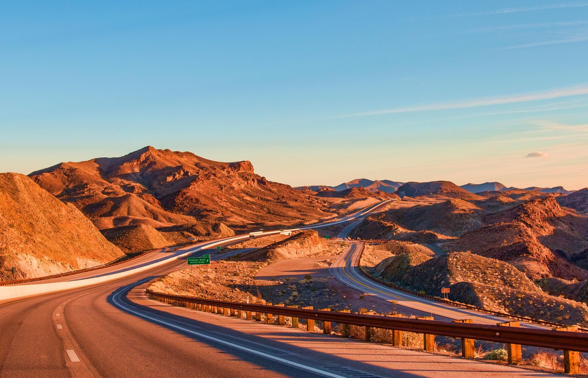 Winding road through a desert landscape with mountains under a blue sky.