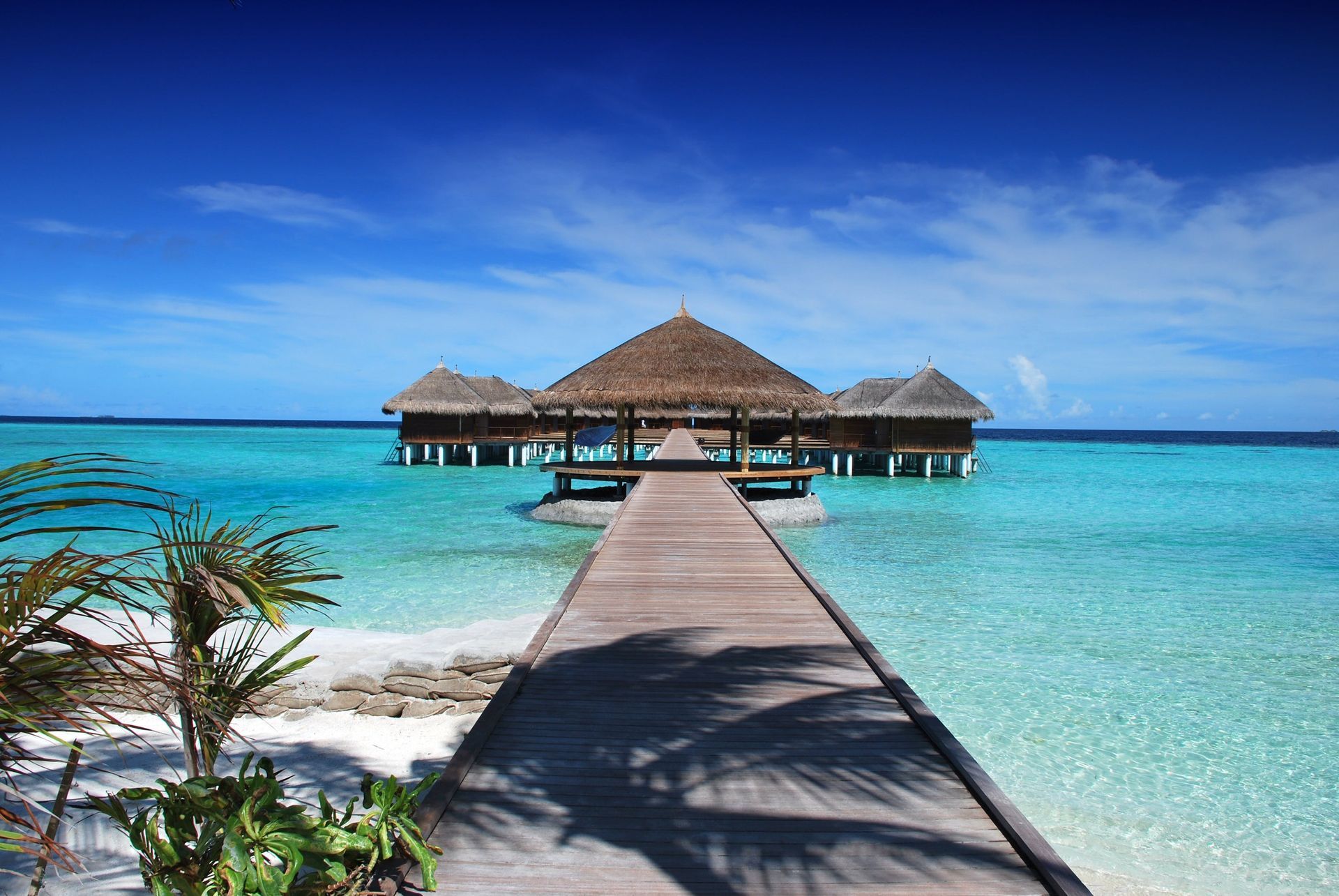 Wooden pier leading to overwater thatched bungalows in a bright turquoise tropical lagoon