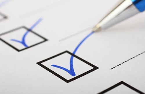 A blue pen finishes marking a blue checkmark in a checkbox on a white paper form.