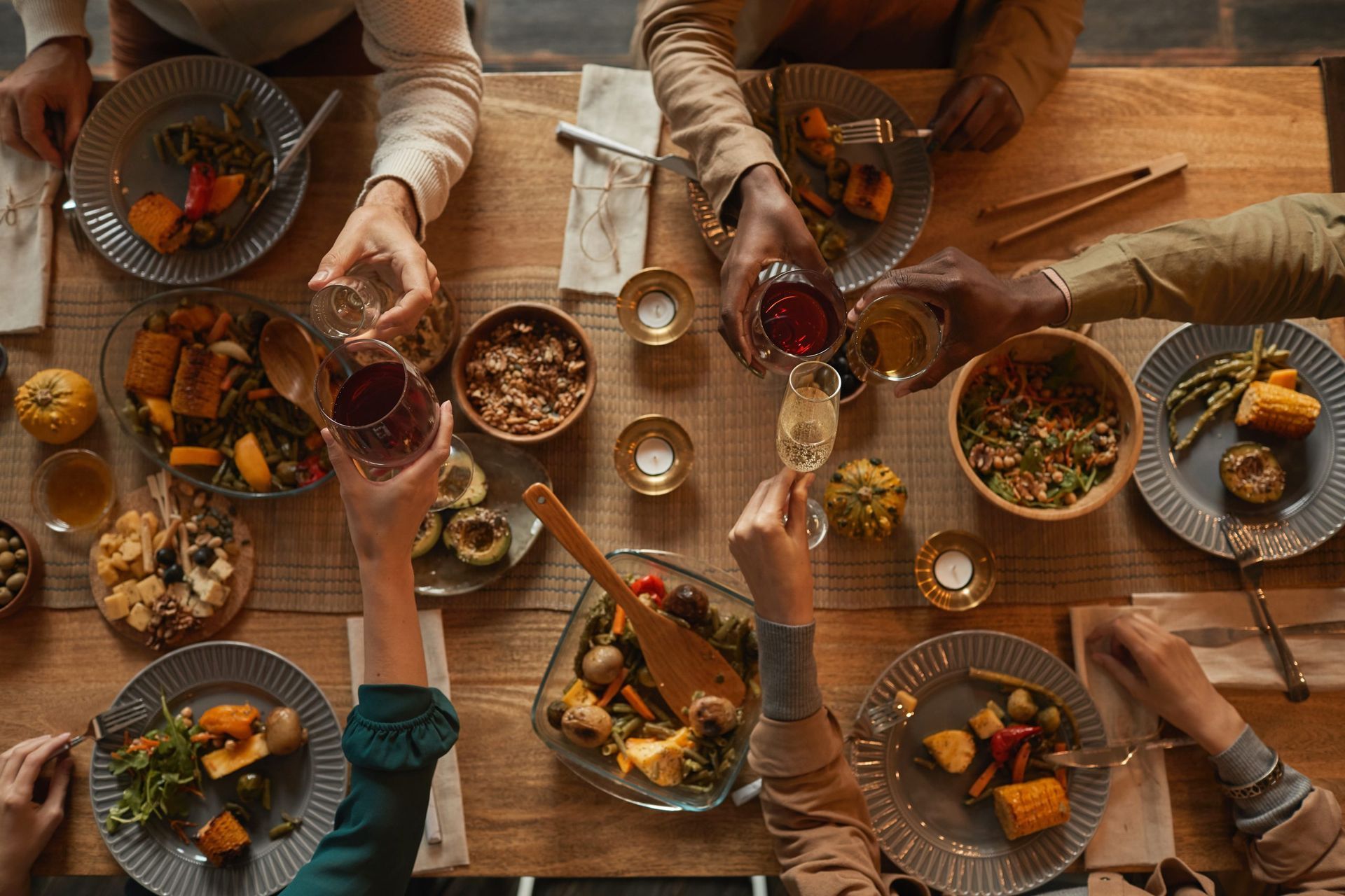 Overhead view of a dinner party with people toasting with wine glasses over a table filled with various dishes.