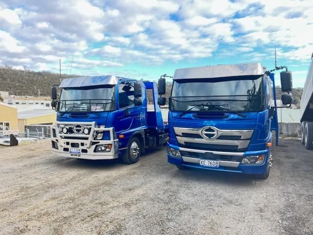 Two blue semi-trucks parked side by side in a gravel lot under a cloudy sky