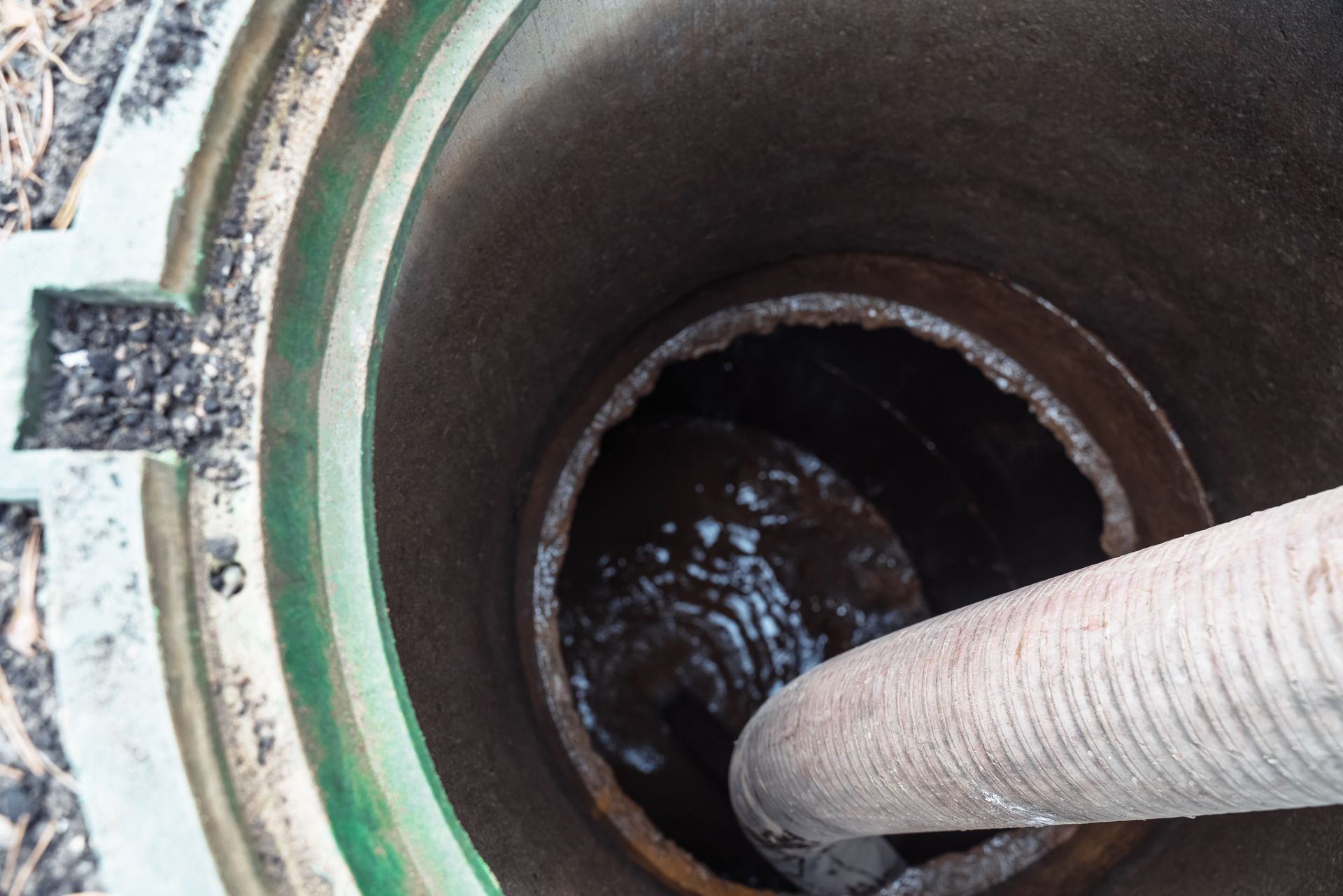 Cylindrical tank opening with a hose inserted, showing a dark liquid inside.