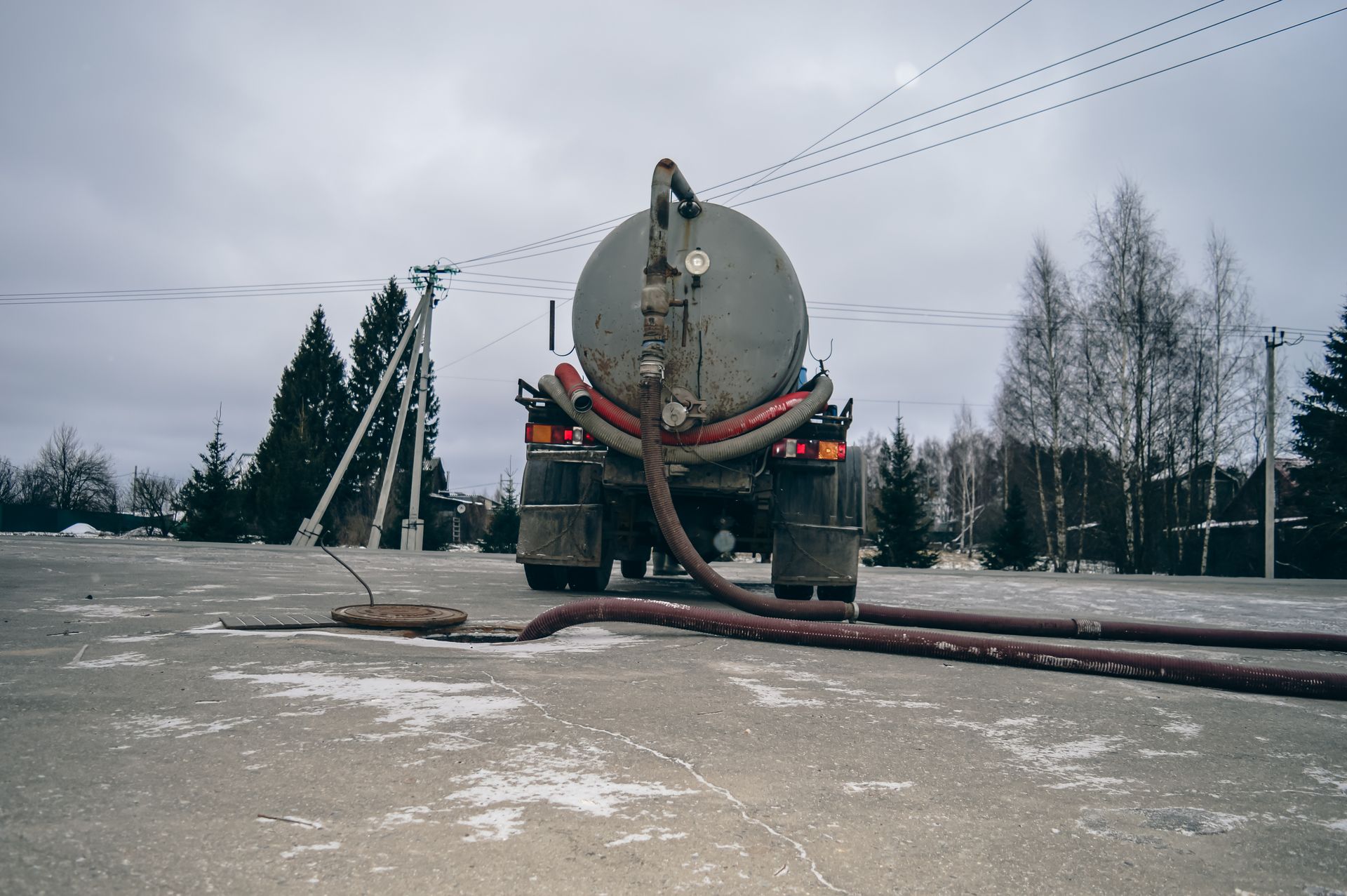 Large tanker truck on a snowy road, hose extending to the ground under a gray winter sky