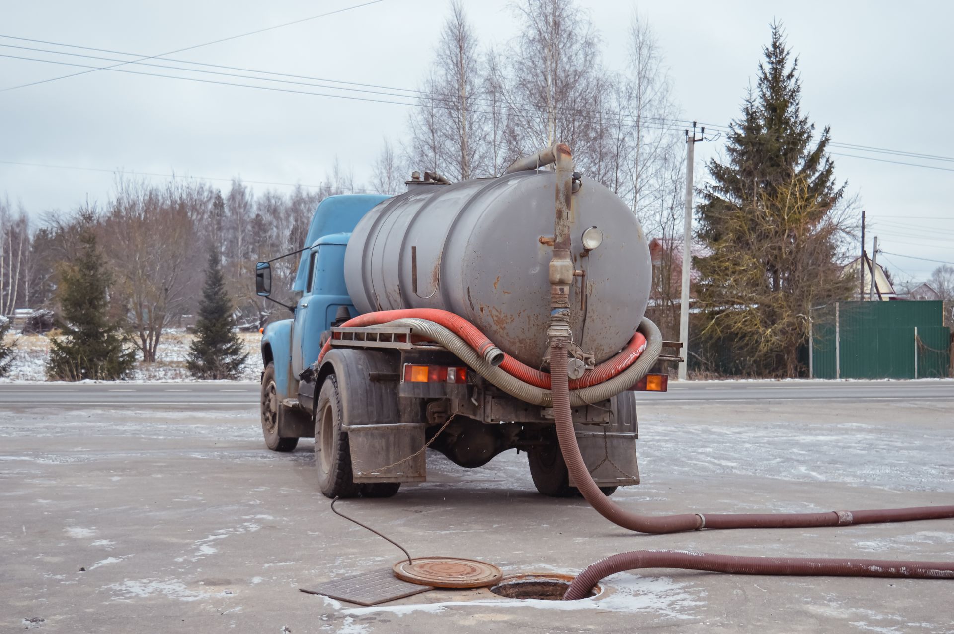 Blue vacuum truck pumping a frozen sewer line in a snowy parking lot