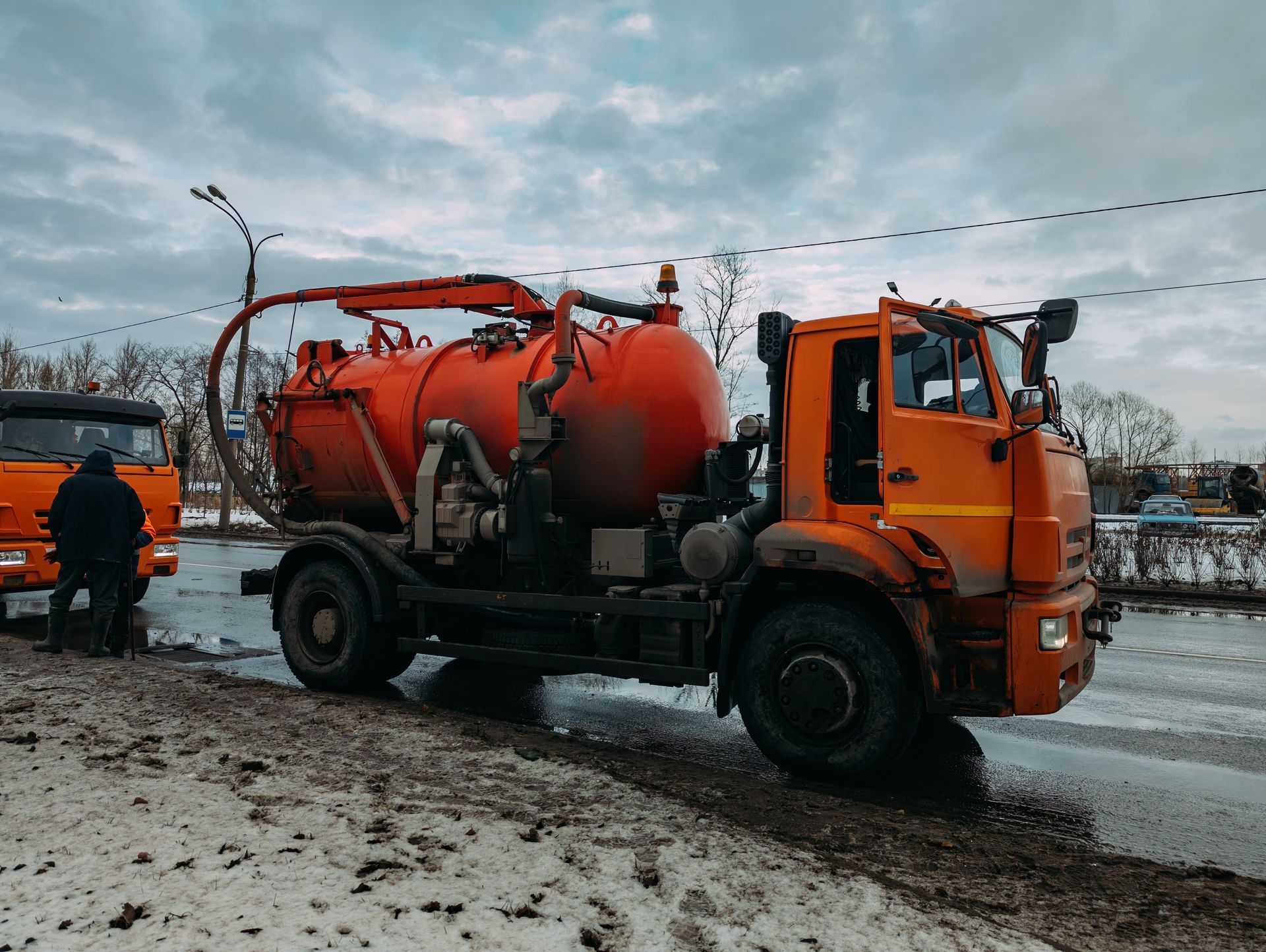 Orange street vacuum truck on a snowy road with a worker beside it.