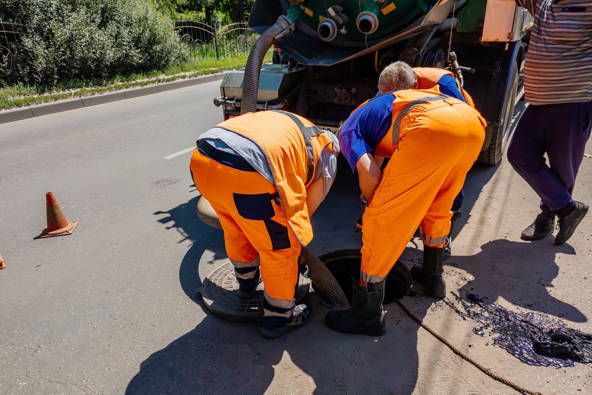 Road workers in orange uniforms repairing pavement beside a utility truck on a roadside.