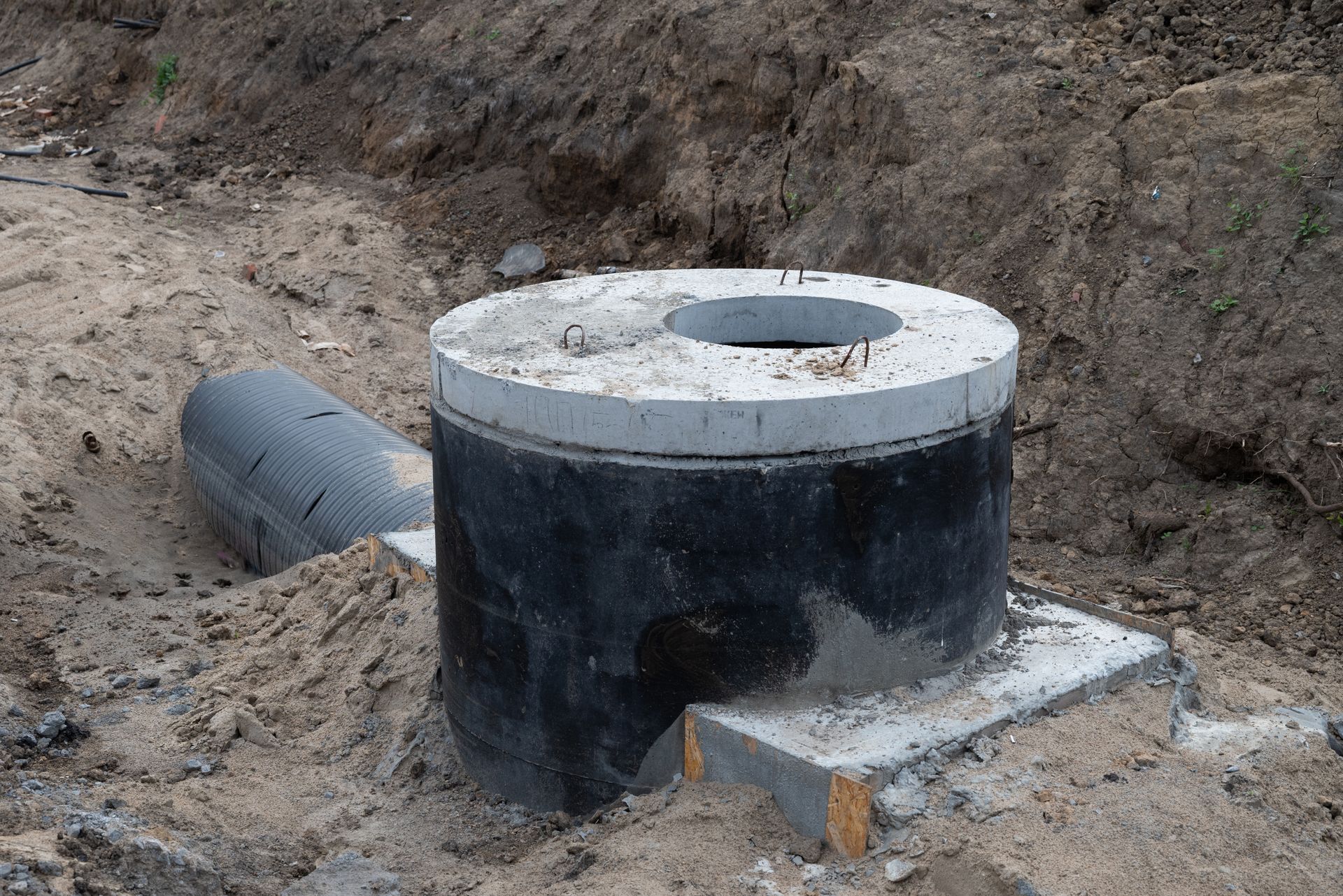 Partially buried black concrete utility chamber with a white circular top at a construction site