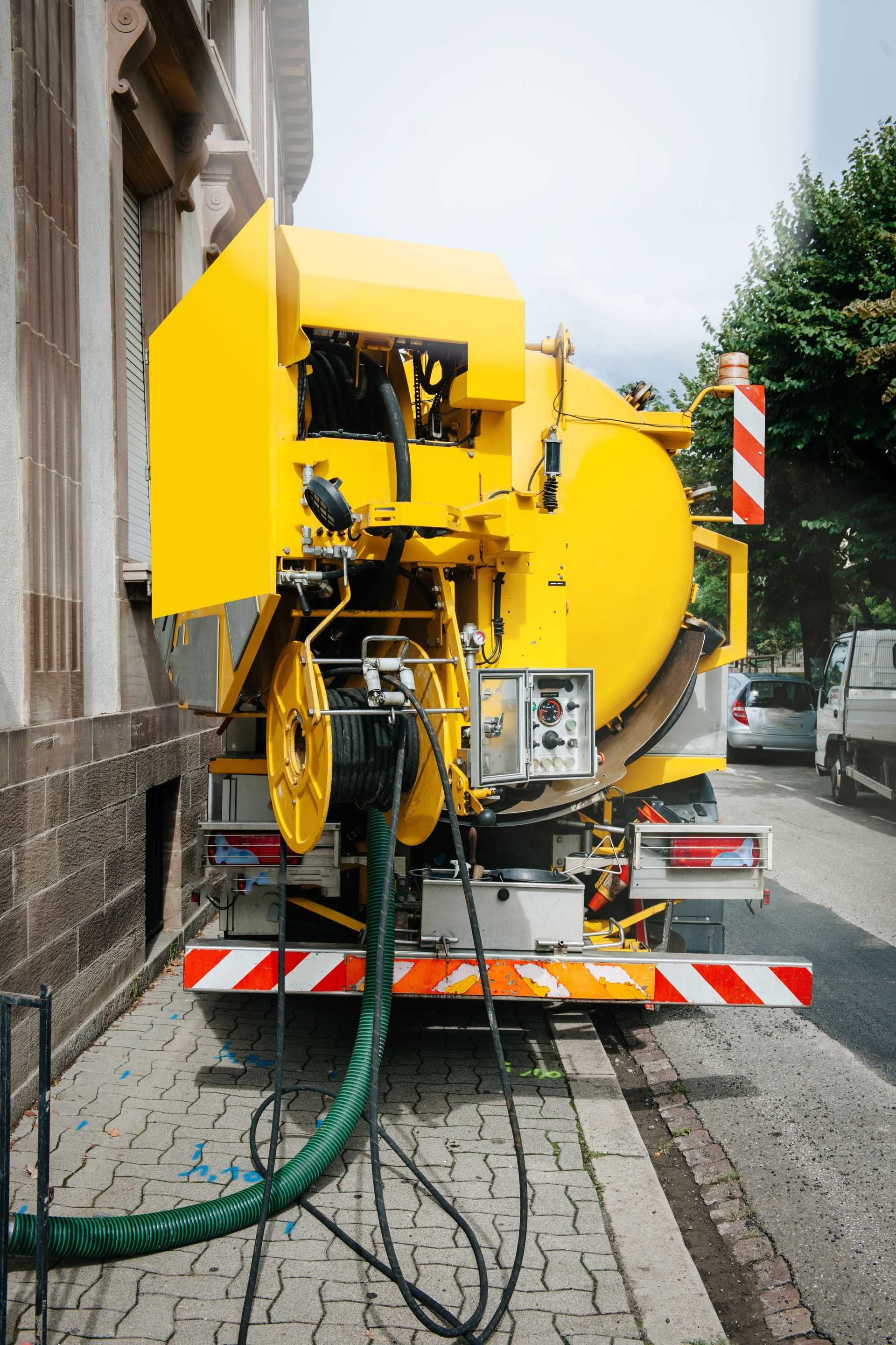 Yellow road-maintenance machine parked on a narrow street, with hoses and striped safety markings.