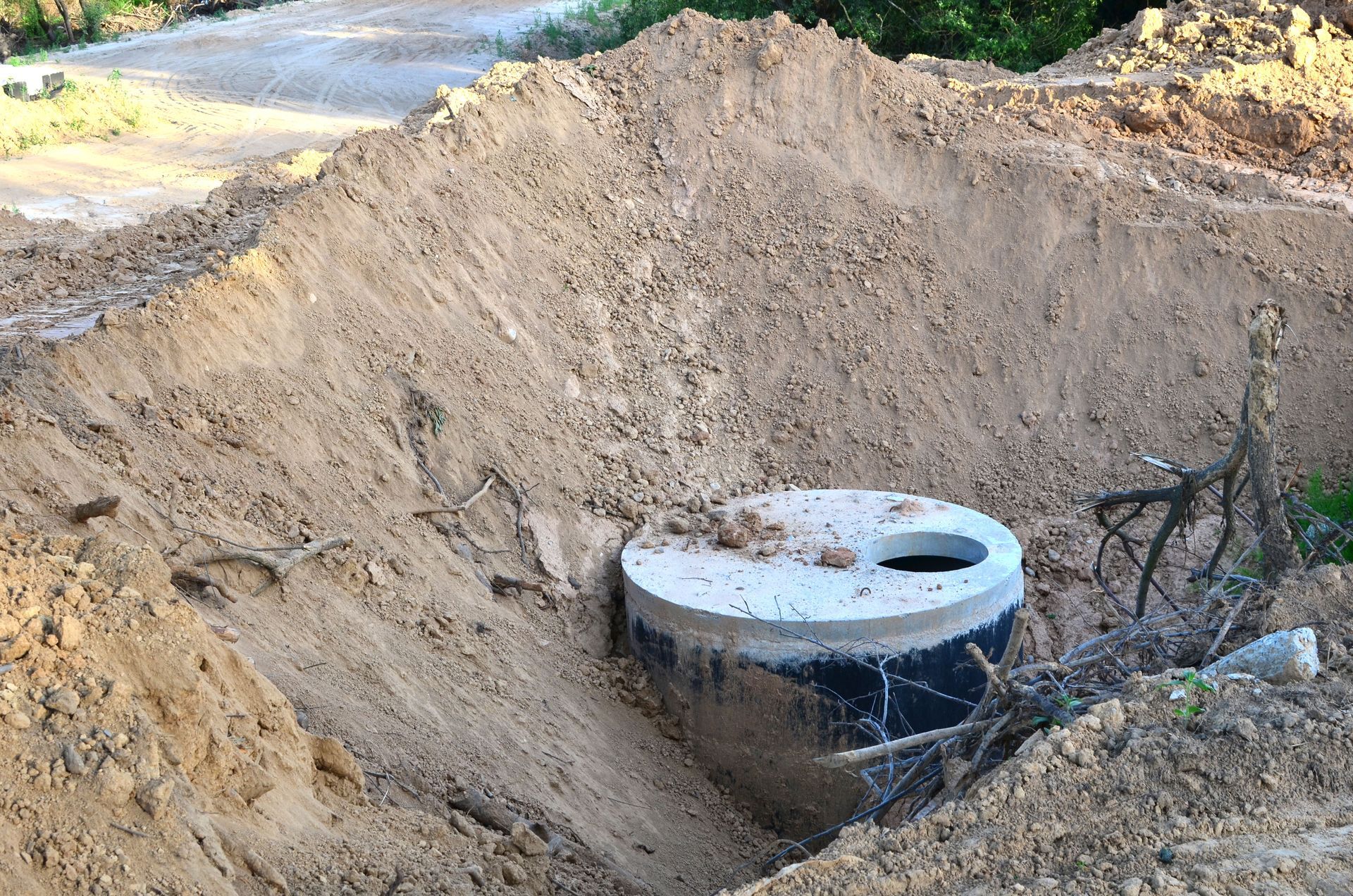 Large dirt excavation with a concrete utility manhole and exposed pipes at the bottom