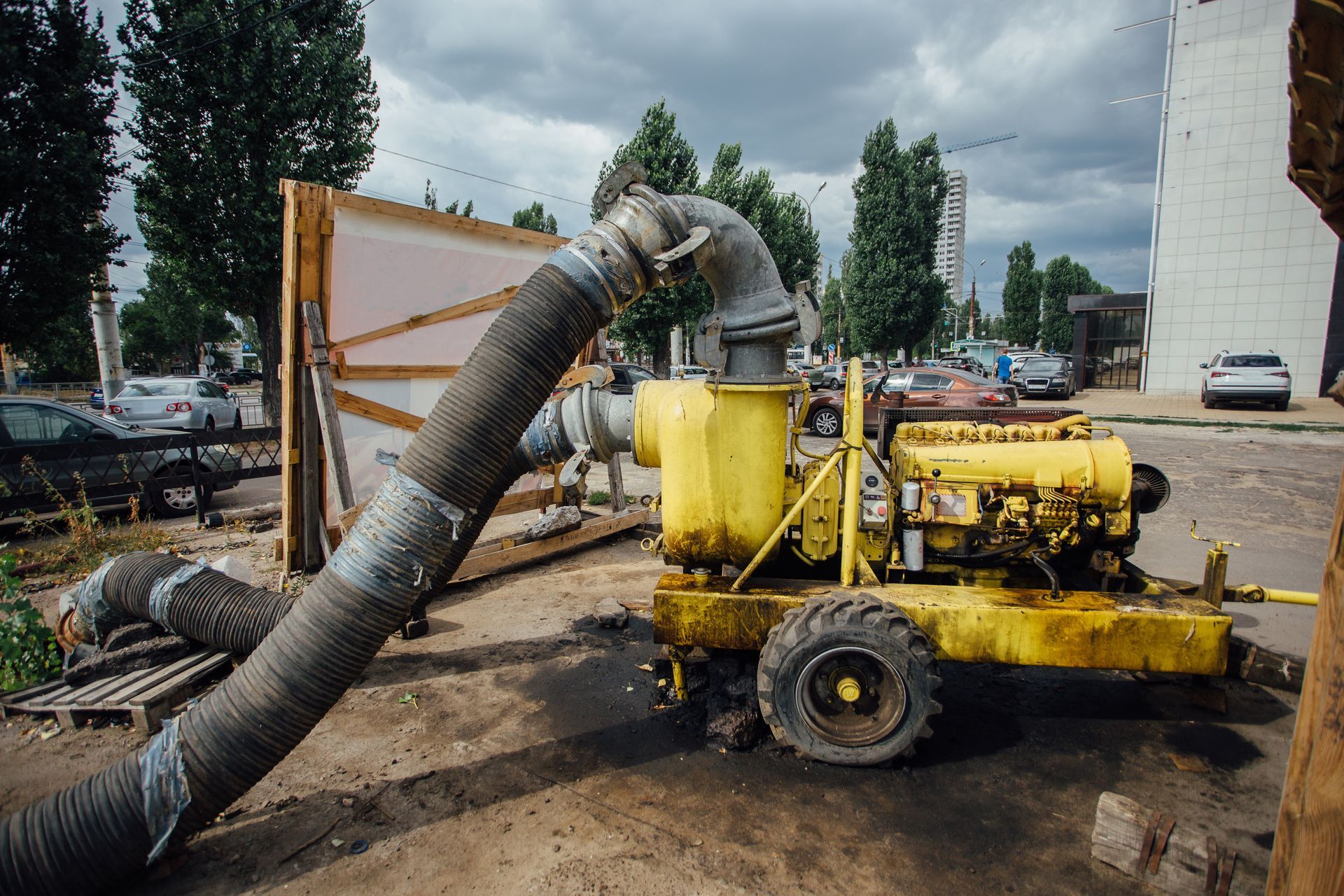 Yellow industrial vacuum truck with a large hose pumping mud at a construction site