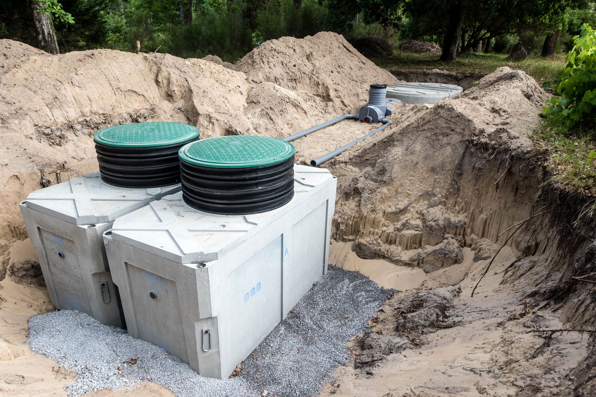 Septic tanks and black lids in a dug-out trench at a construction site, surrounded by dirt and gravel