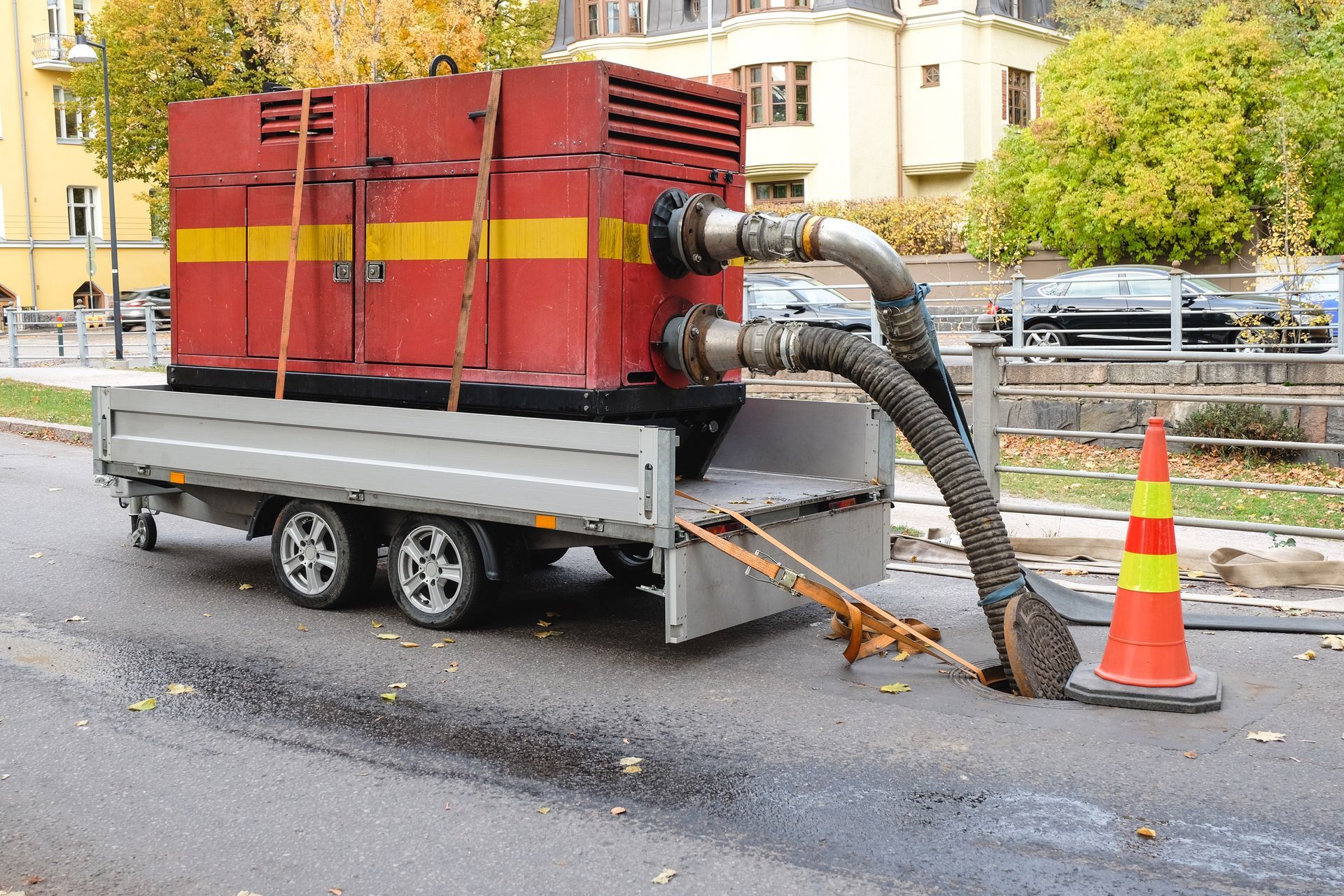 Mobile industrial vacuum on a trailer suctioning water from the street beside a traffic cone
