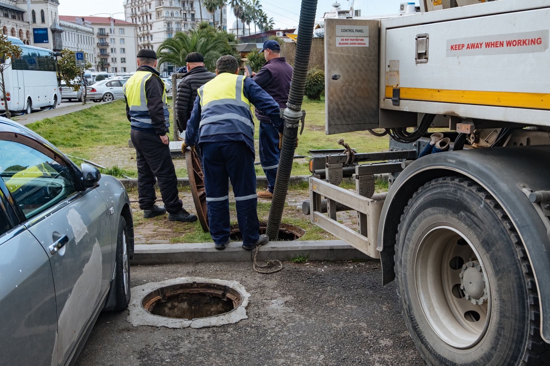 Workers inspect a street manhole beside a truck in an urban road scene
