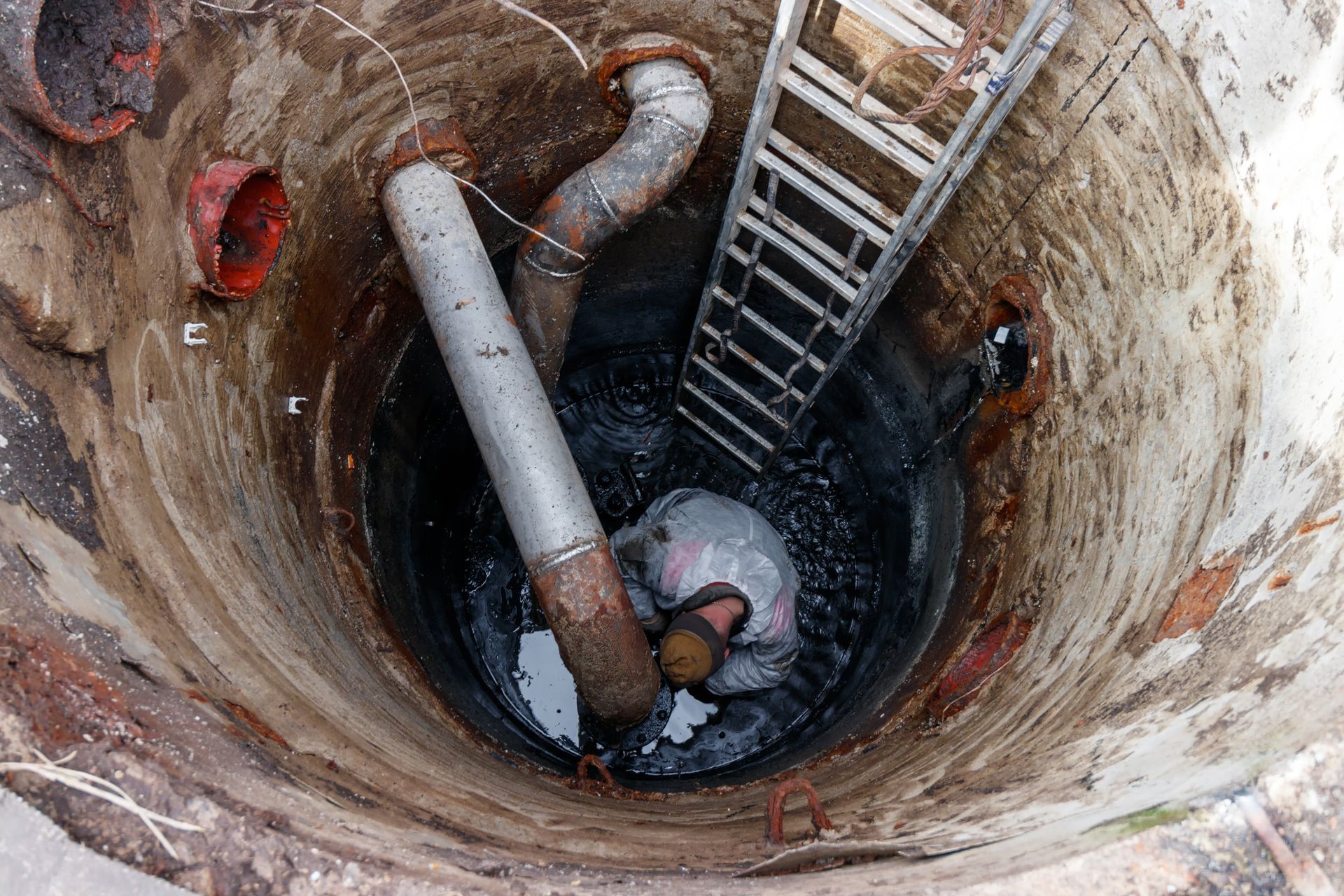 Worker inside a deep concrete well beside a ladder and large pipes