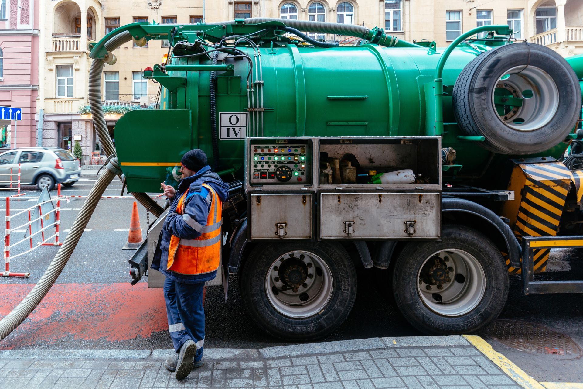 Worker beside large green sewer vacuum truck on city street