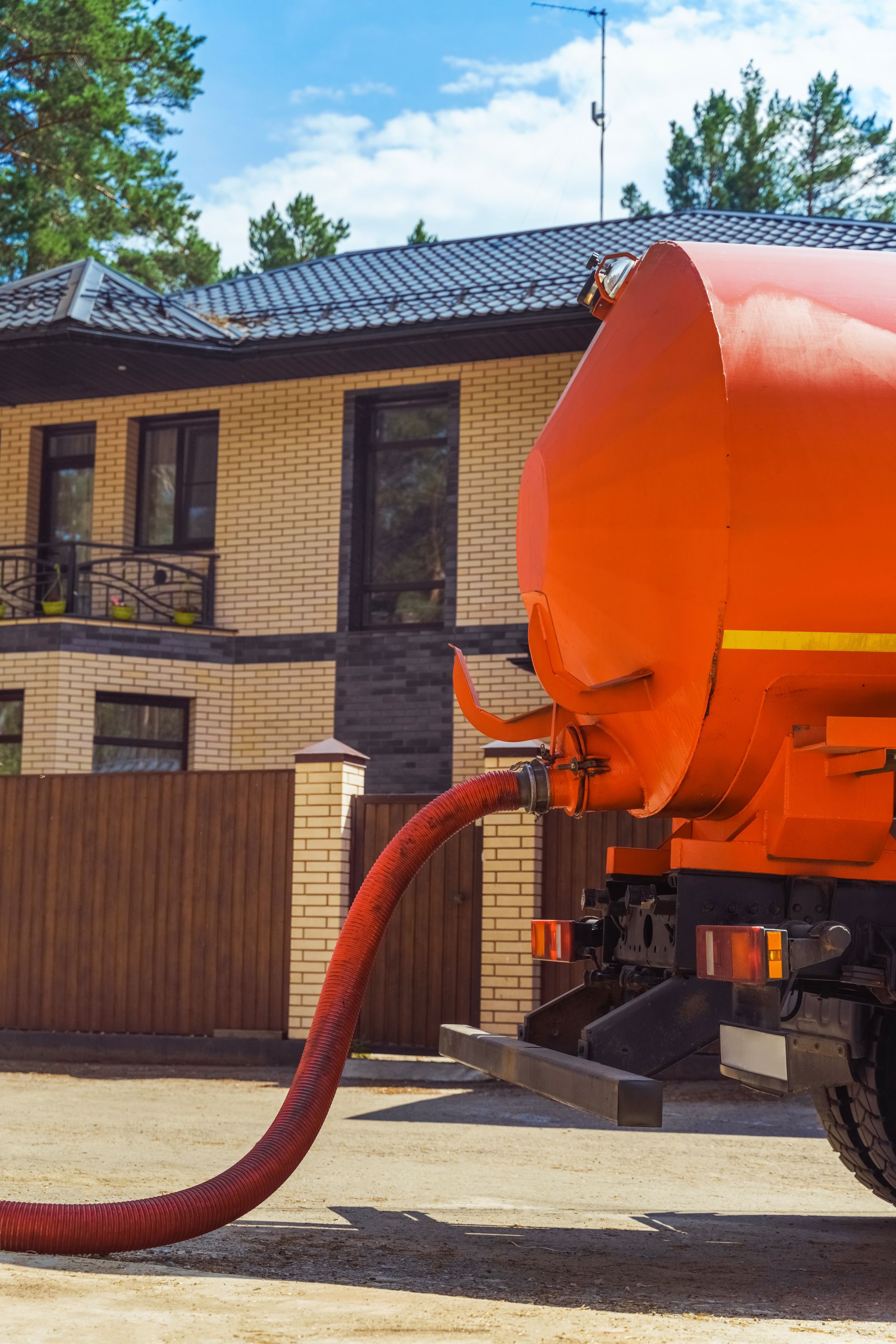 Orange vacuum truck hose cleaning a residential street in front of a brick house