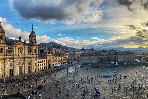 Vista en ángulo alto de la Plaza de Bolívar de Bogotá con la Catedral Primada, edificios coloniales y gente al atardecer.