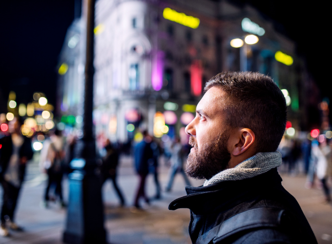 A man with a beard is standing on a city street at night.